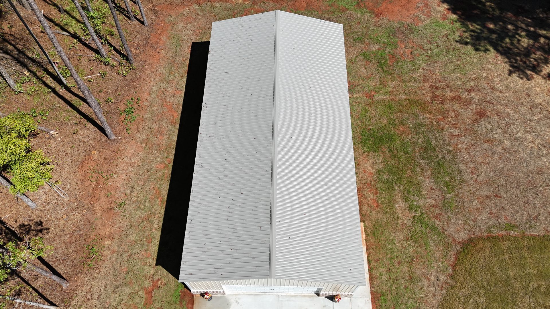 Overhead view of a building with a gray, corrugated metal roof surrounded by brown and green ground.