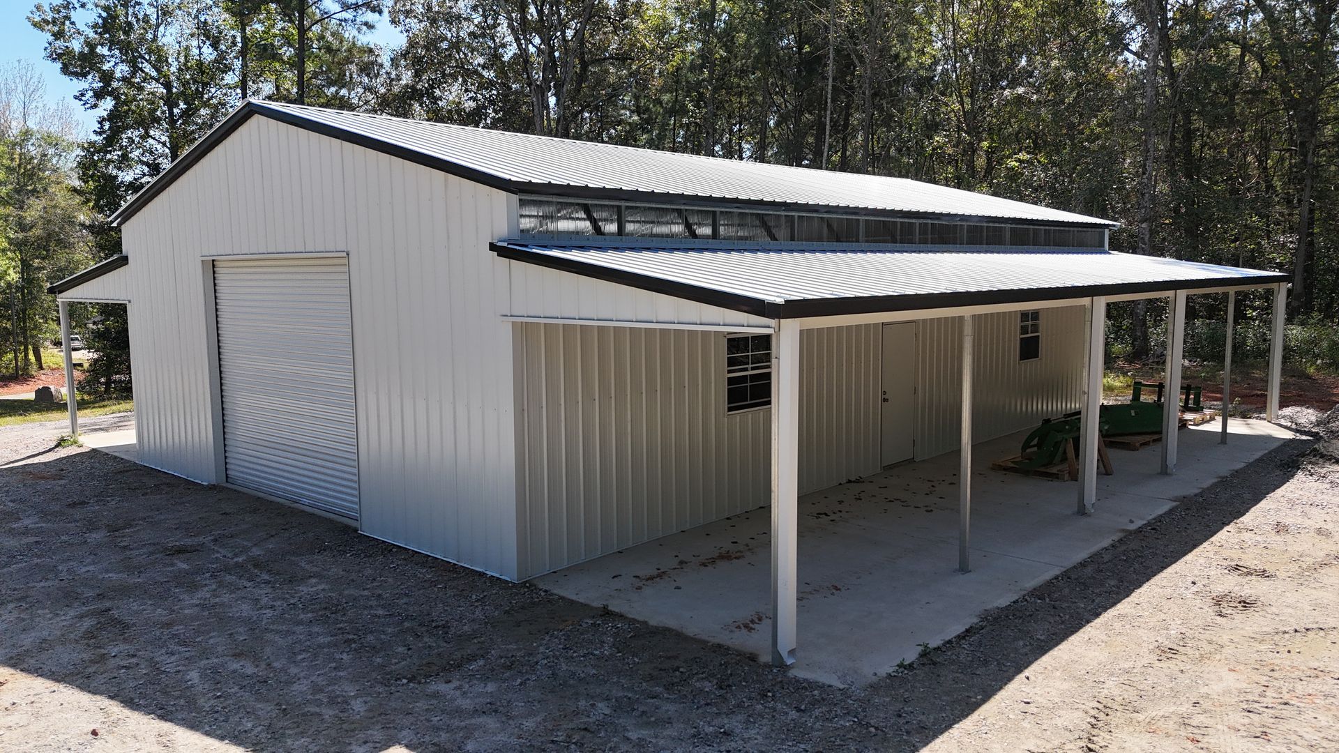 White metal barn with porch and garage door; situated on gravel with trees in the background.
