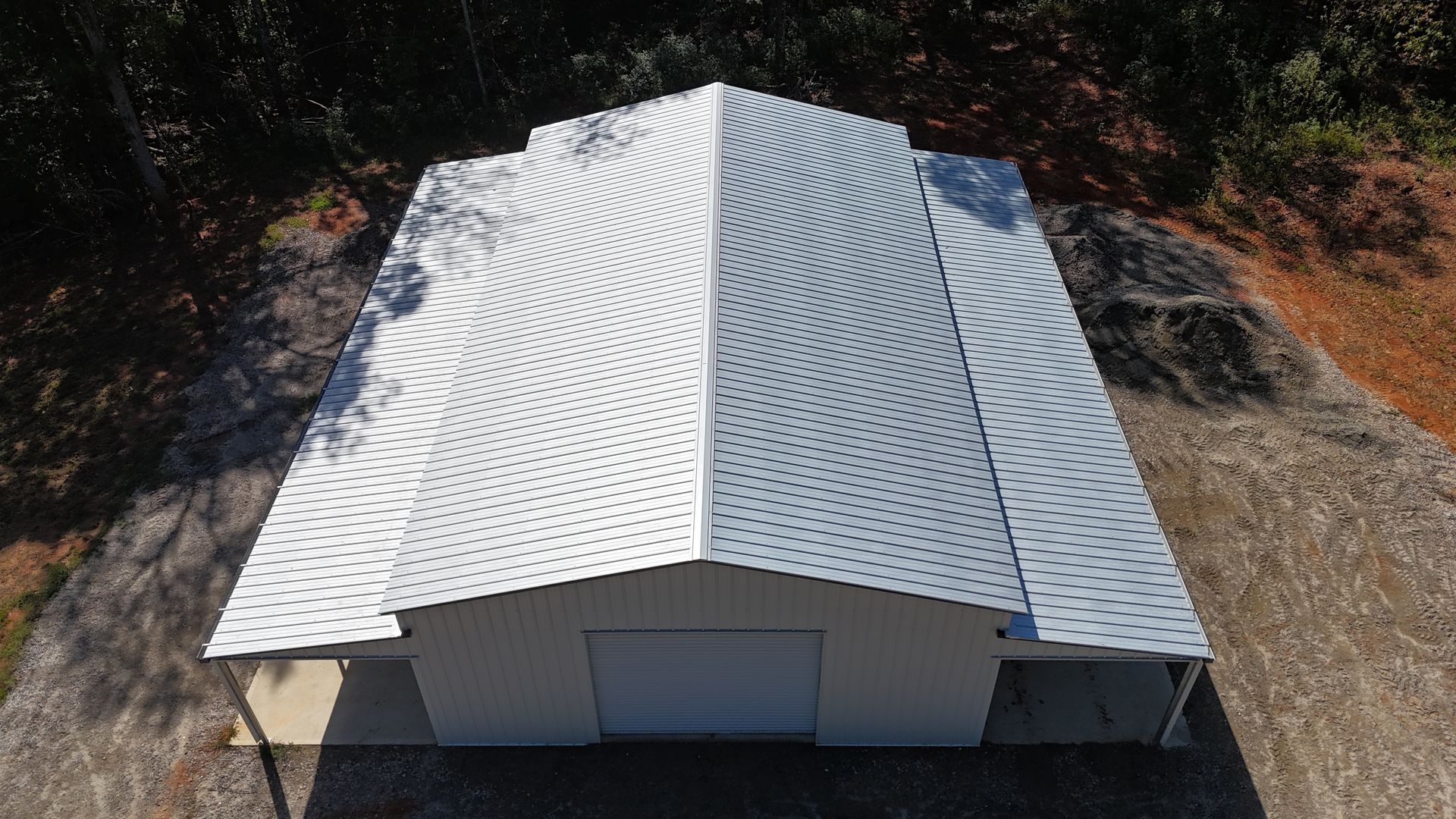White metal-roofed building with swirling pattern, fronted by a closed garage door, set on concrete in a wooded area.