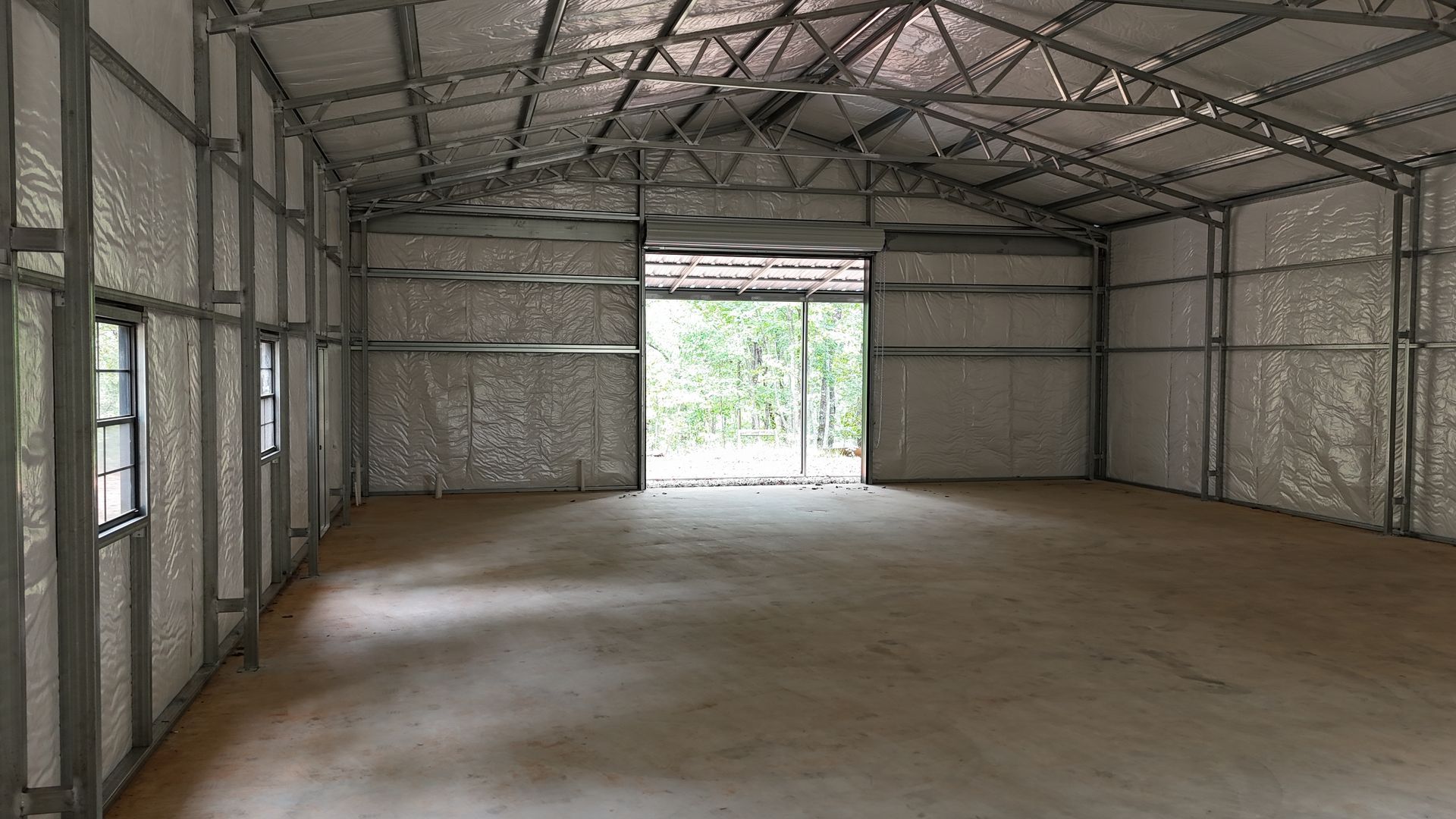 Empty metal framed building interior with open door and concrete floor.