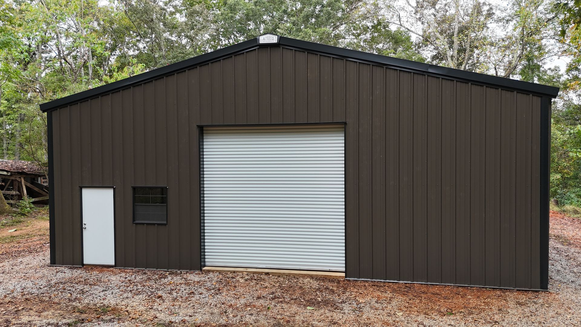 Brown metal building with a large garage door and a small entry door.