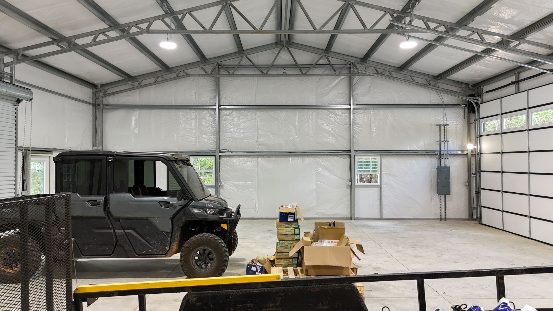 Inside a spacious, light-filled metal building: a utility vehicle, boxes, and a workbench.