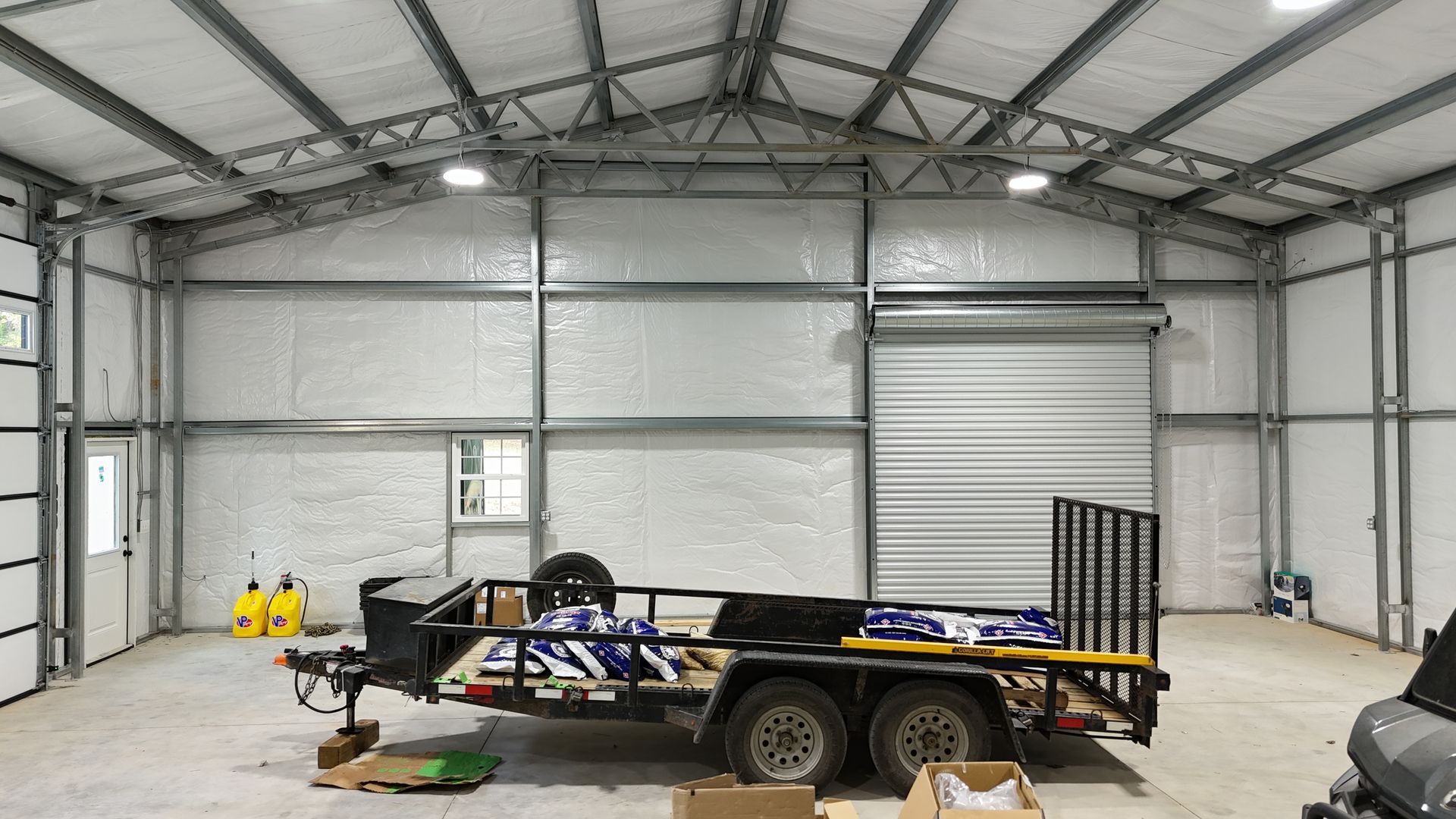 Interior of a metal building with a trailer, door, window, and lights.