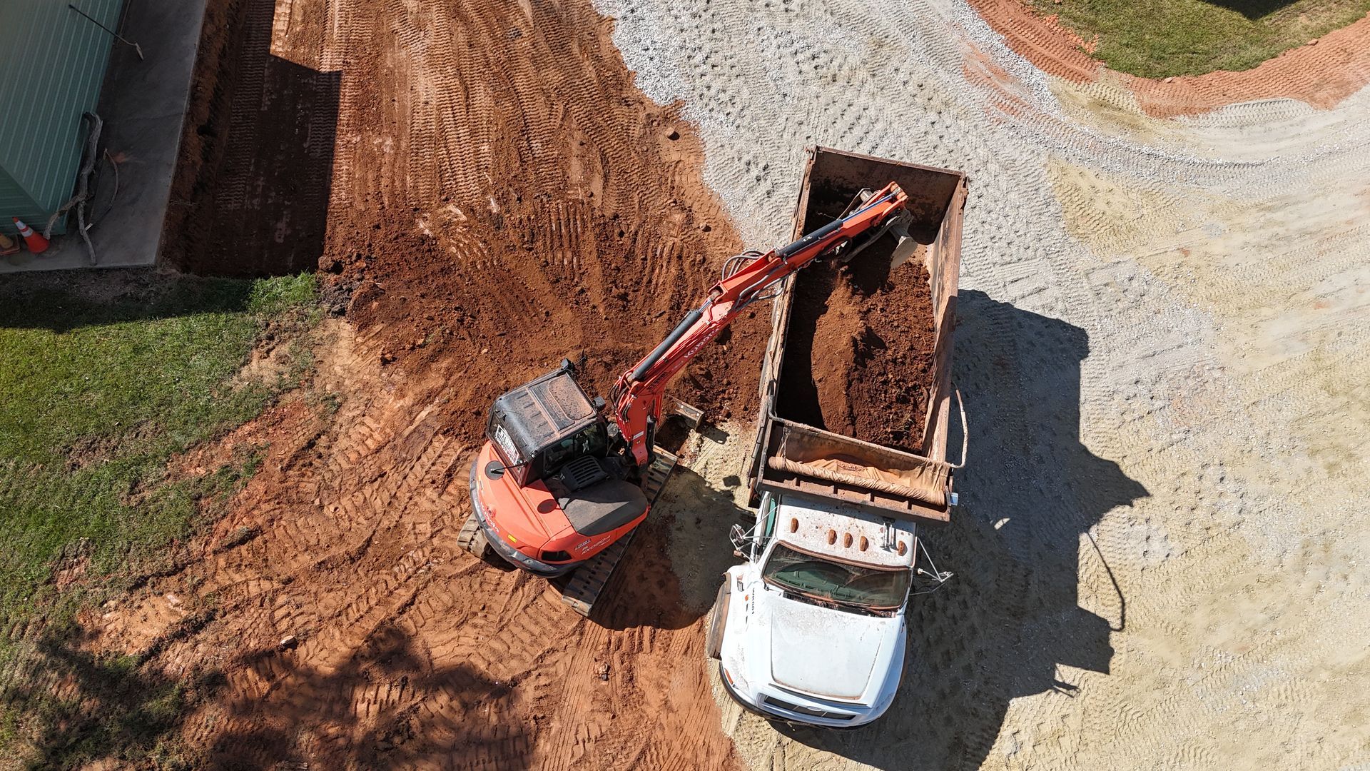 Excavator loading dirt into a white dump truck, on a dirt and gravel surface.
