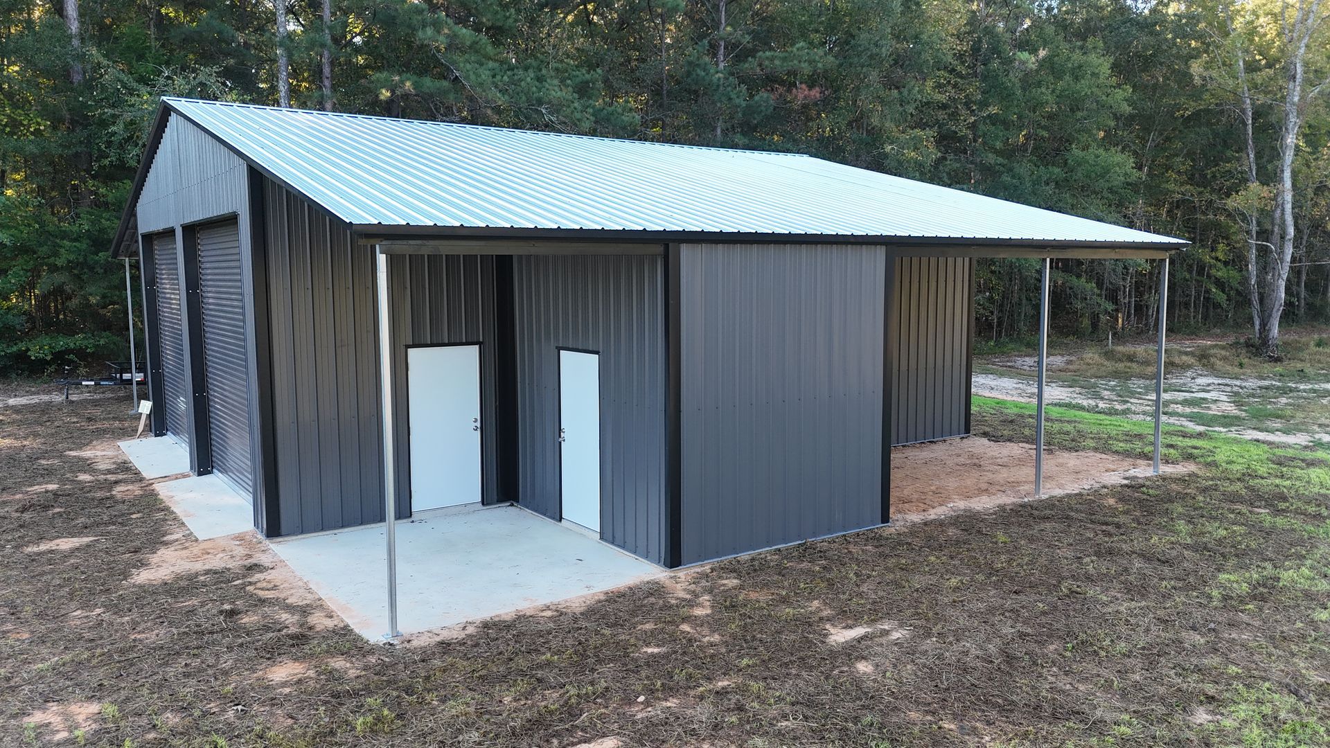 Gray metal barn with a corrugated silver roof, concrete slab, and covered porch.
