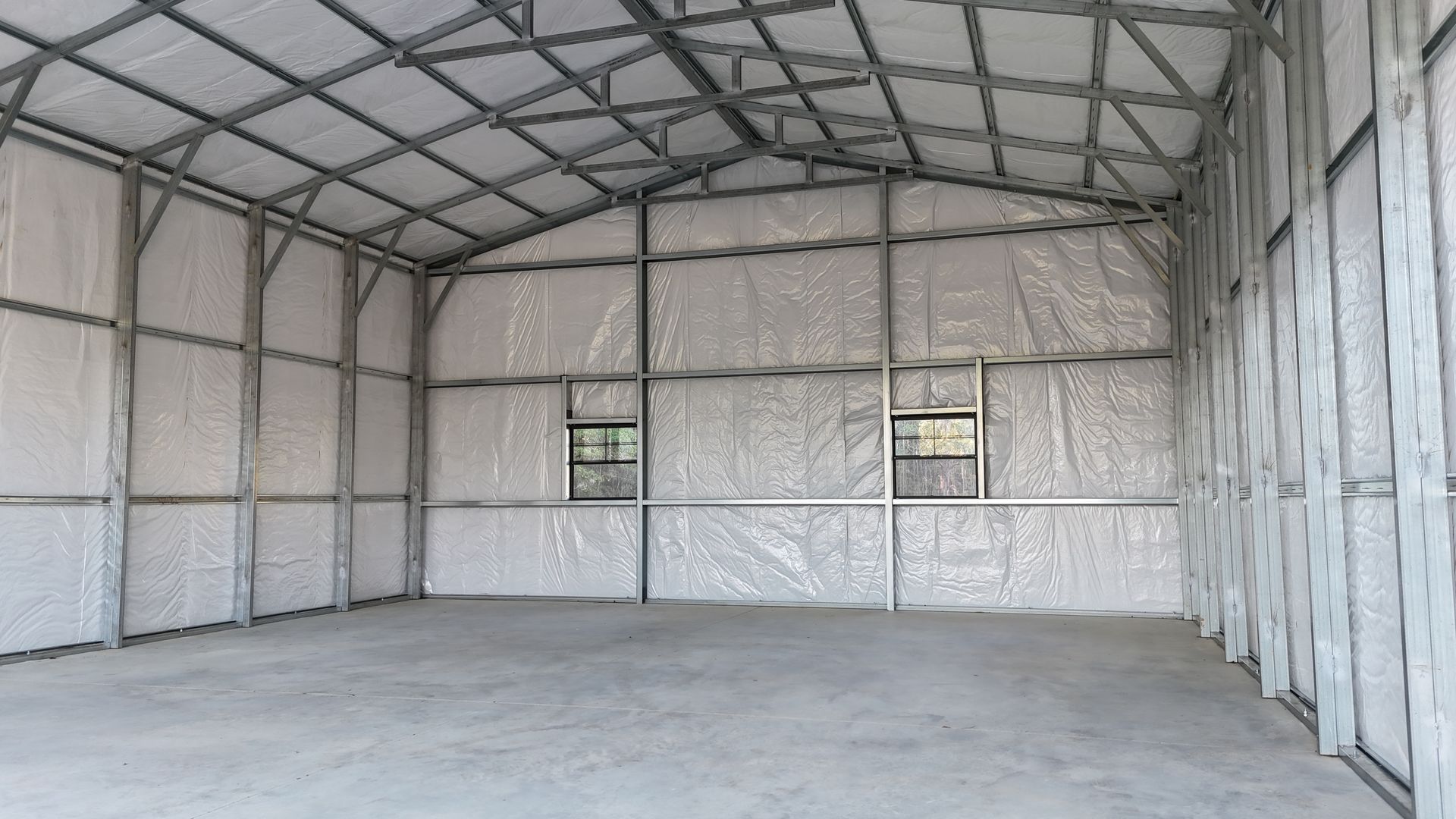 Empty metal frame building with insulation, windows, and concrete floor.