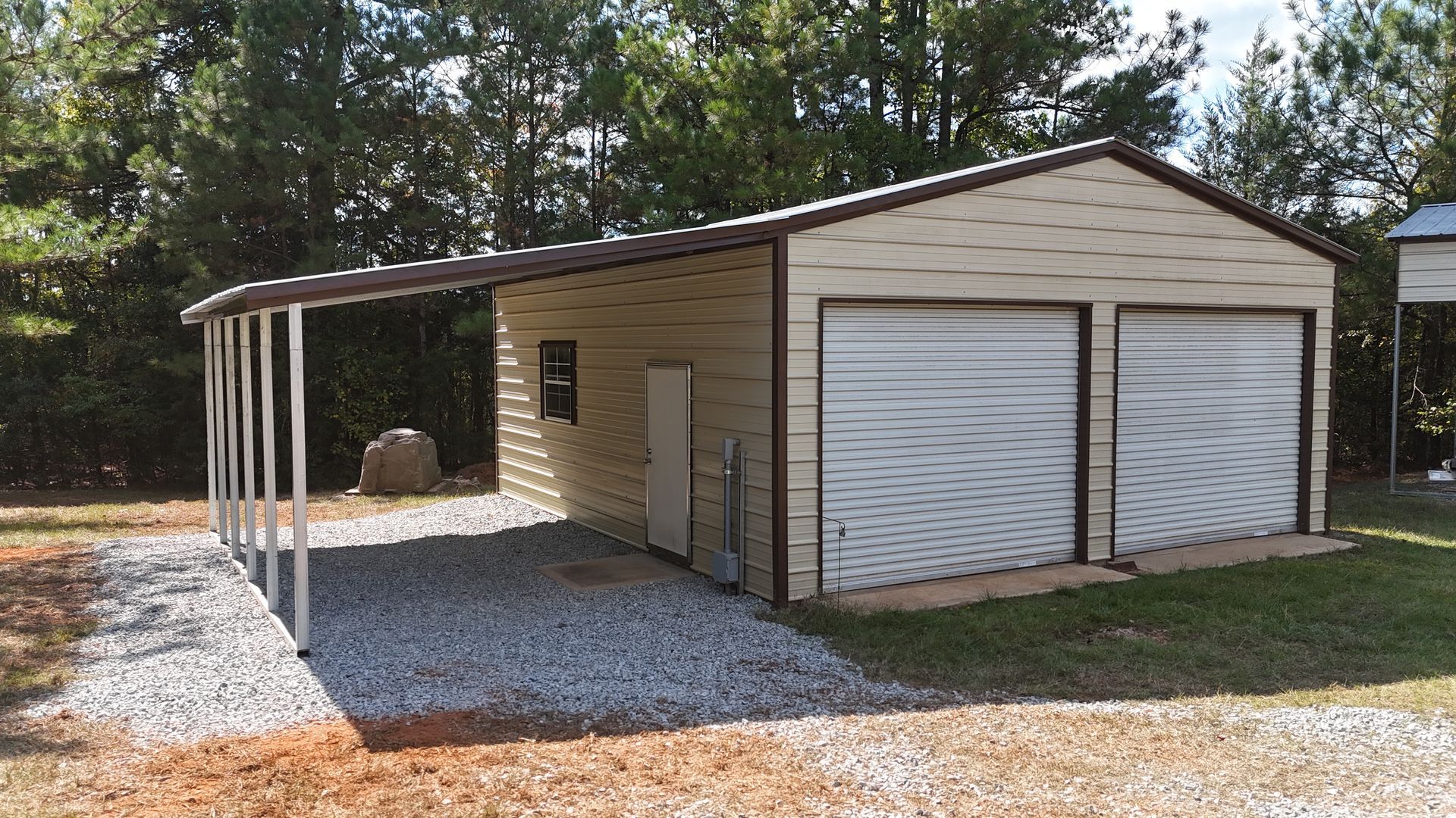 Tan and brown metal garage with two doors and a carport. Gravel driveway.