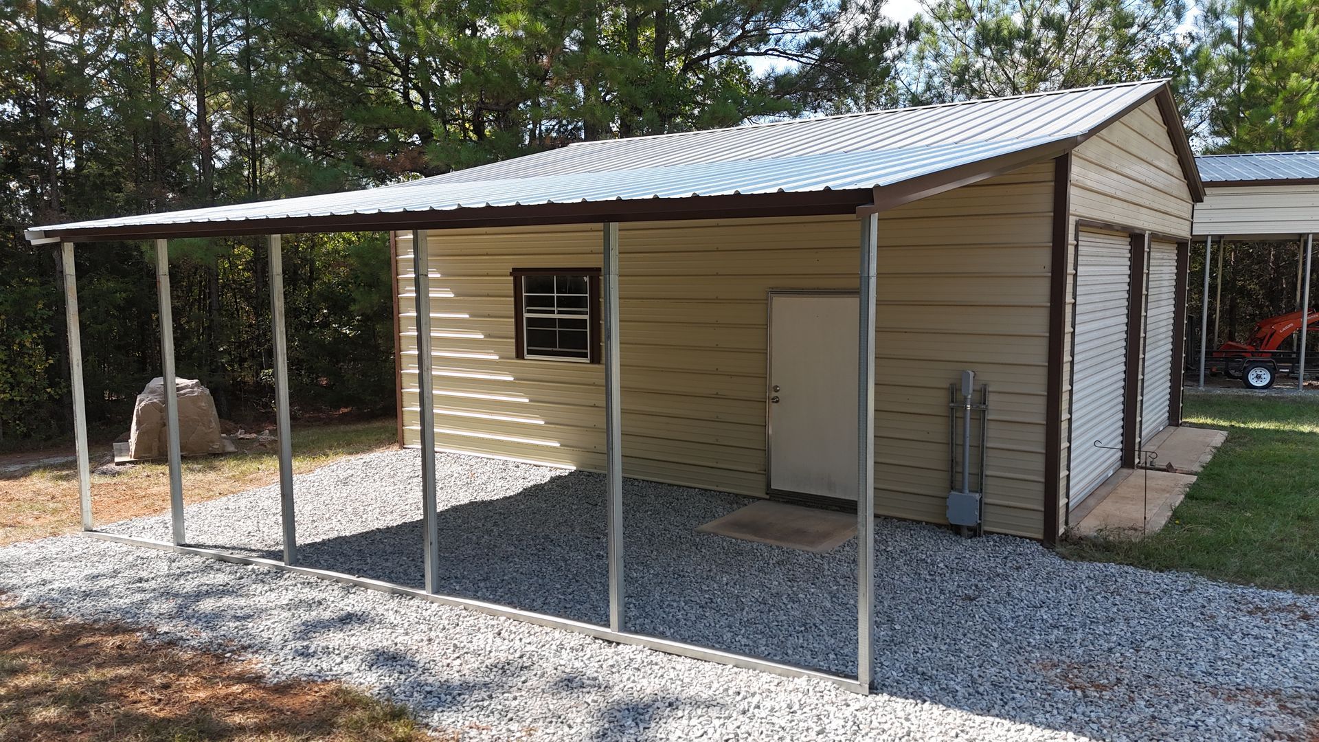 Beige metal shed with carport and gravel driveway.