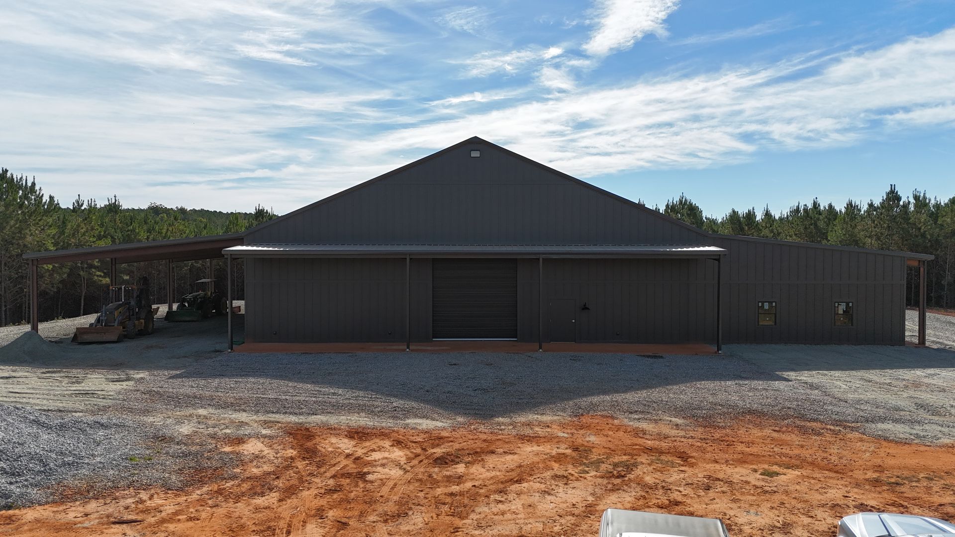 Dark gray metal barn-style building with a gravel driveway under a blue sky.