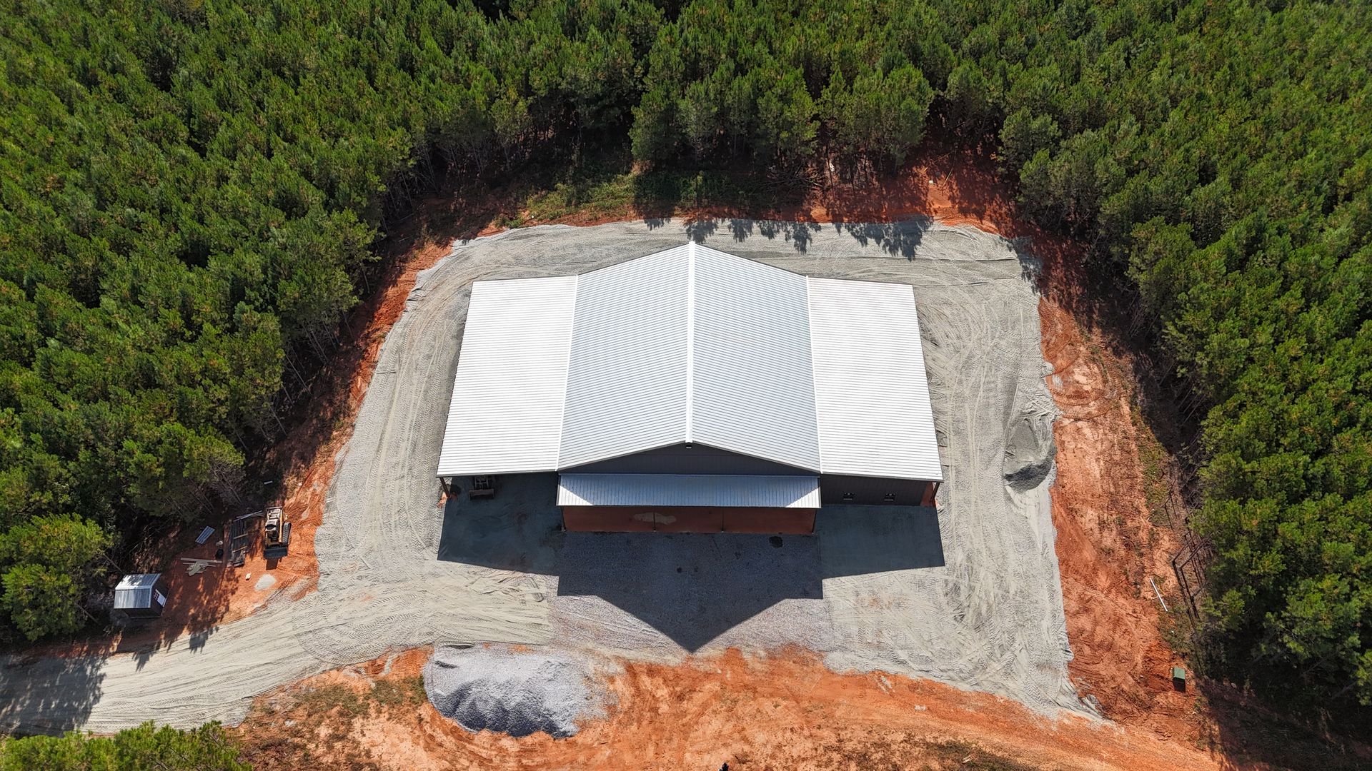 Aerial view of a metal-roofed building surrounded by trees and a gravel perimeter.