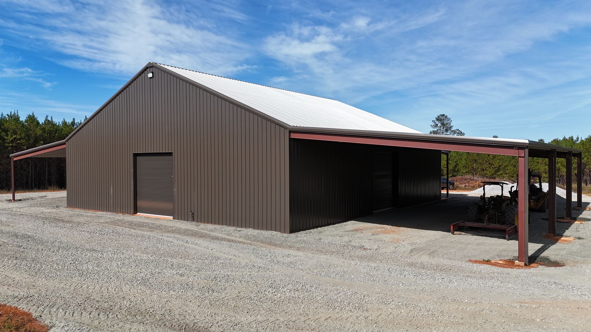 Brown metal building with attached brown canopy, white roof, gravel ground, blue sky.