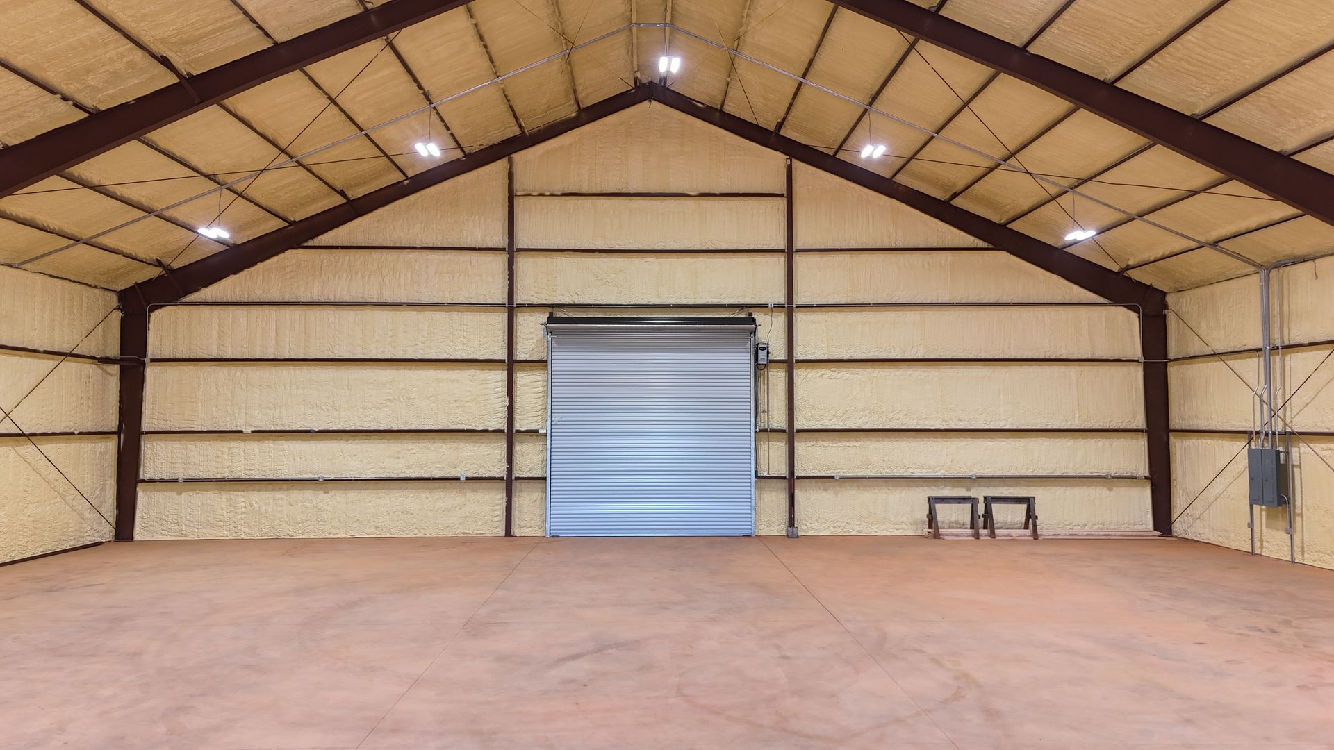 Interior of an empty warehouse with a roll-up door, brown steel beams, and tan insulated walls.