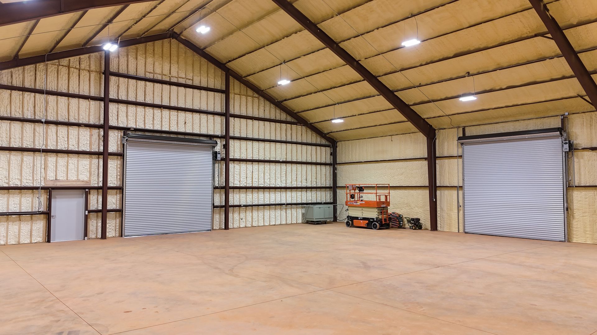 Interior of a metal warehouse with roll-up doors, insulated walls and ceiling, and a concrete floor.