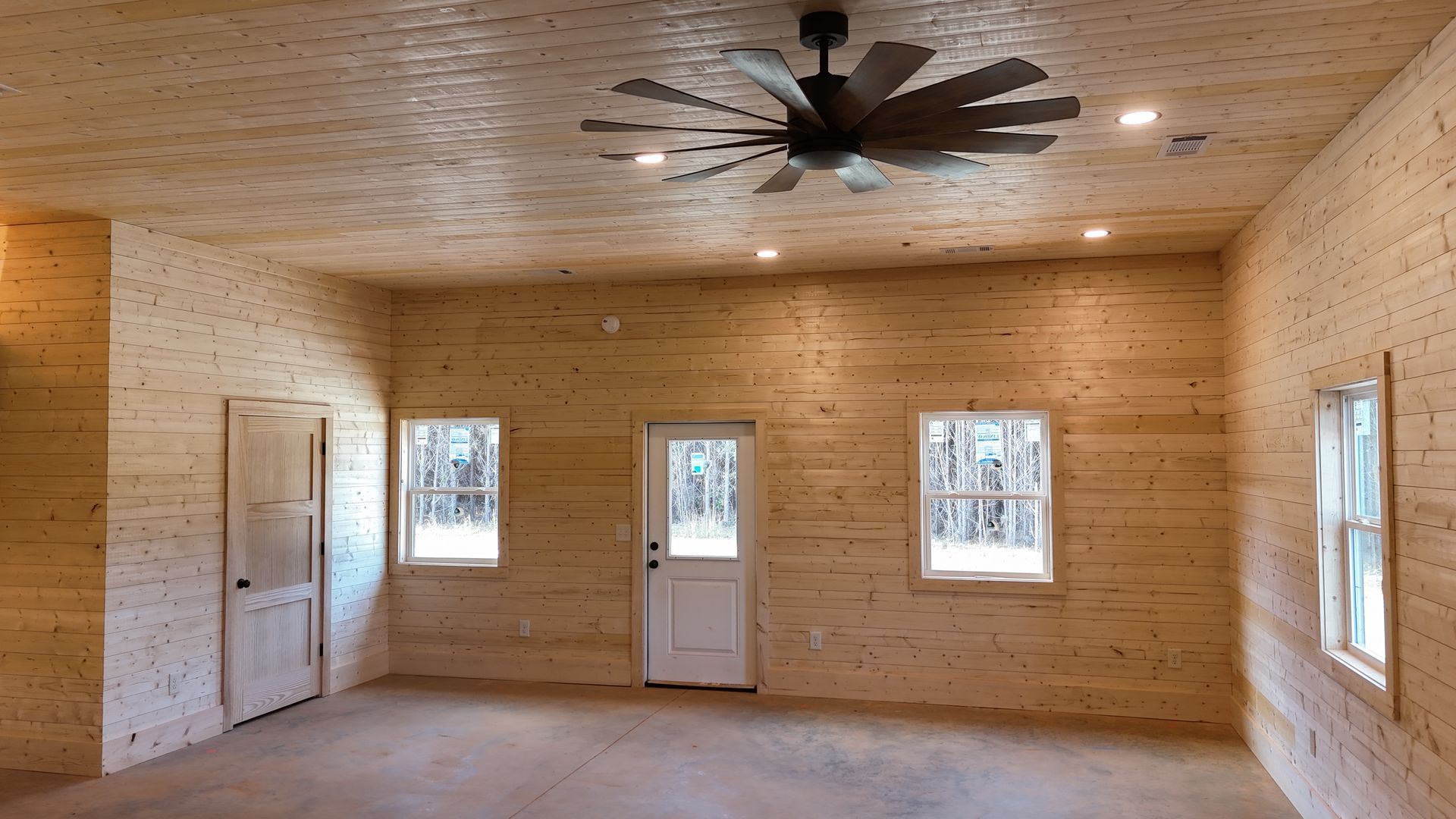 Interior of a room with wood paneled walls, a door, windows, and ceiling fan.