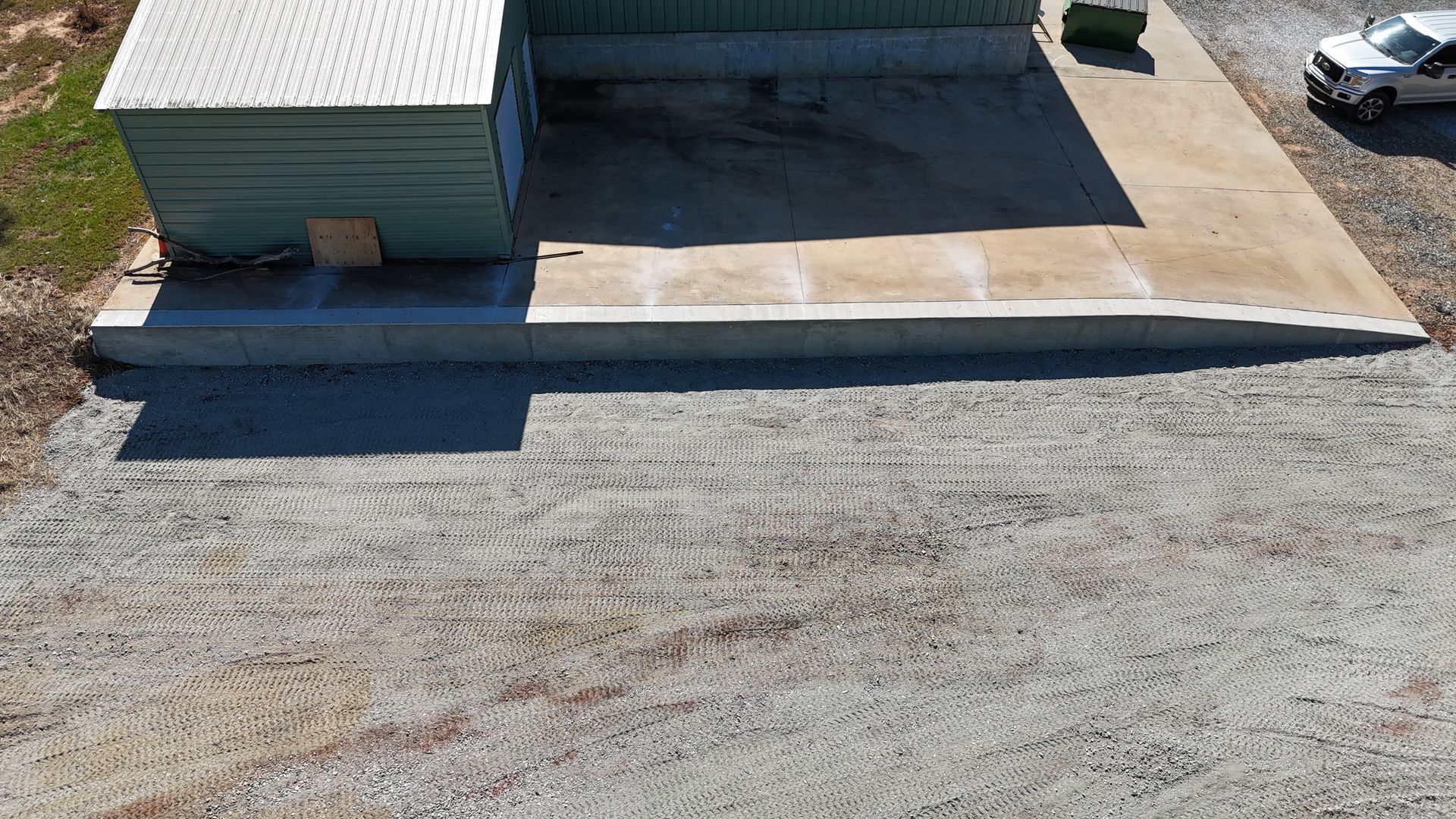 Green metal building with concrete ramp, gravel driveway, and white truck.