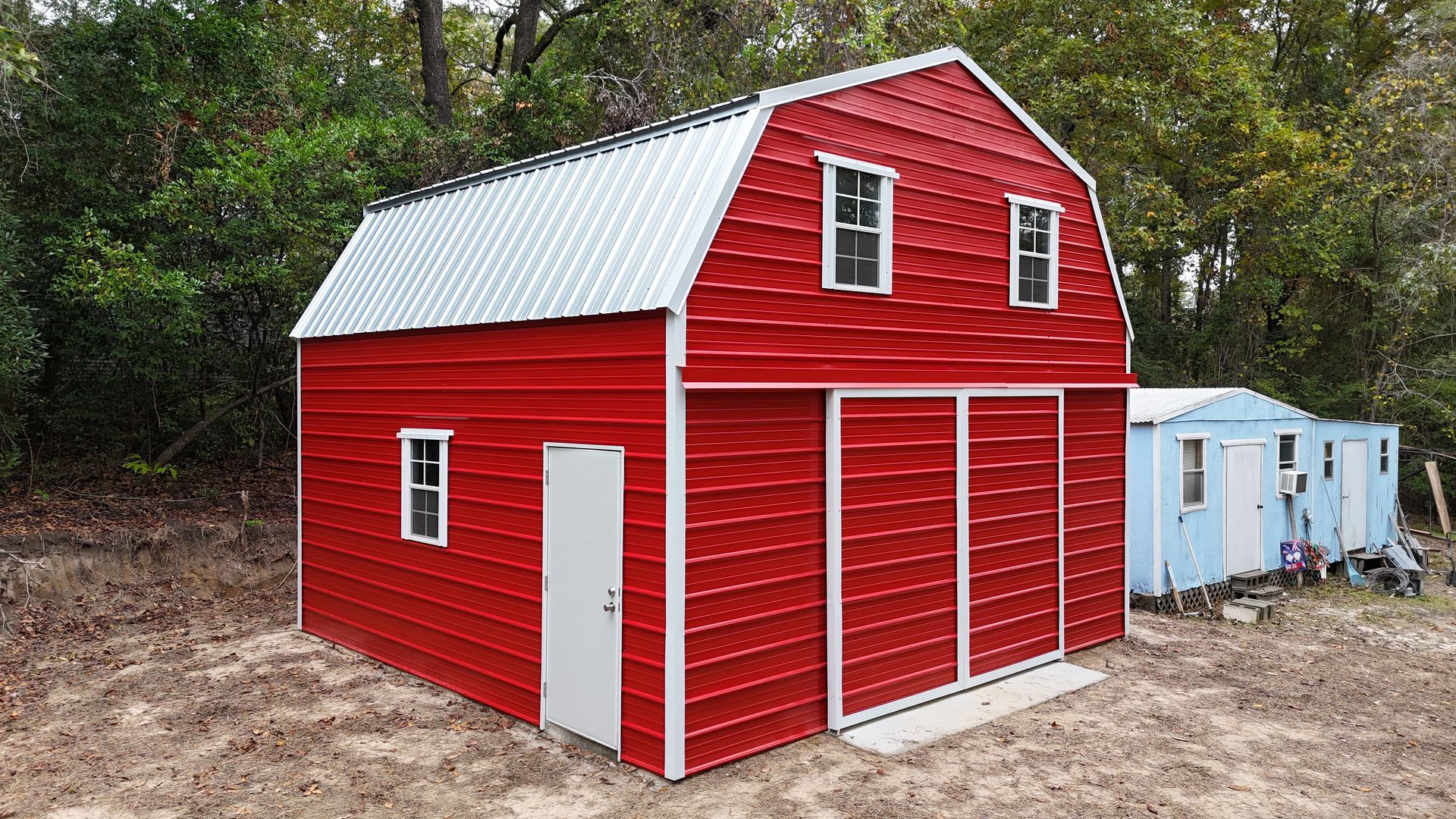 Red barn-style shed with white trim and sliding doors, two small windows on top level, another on the side.