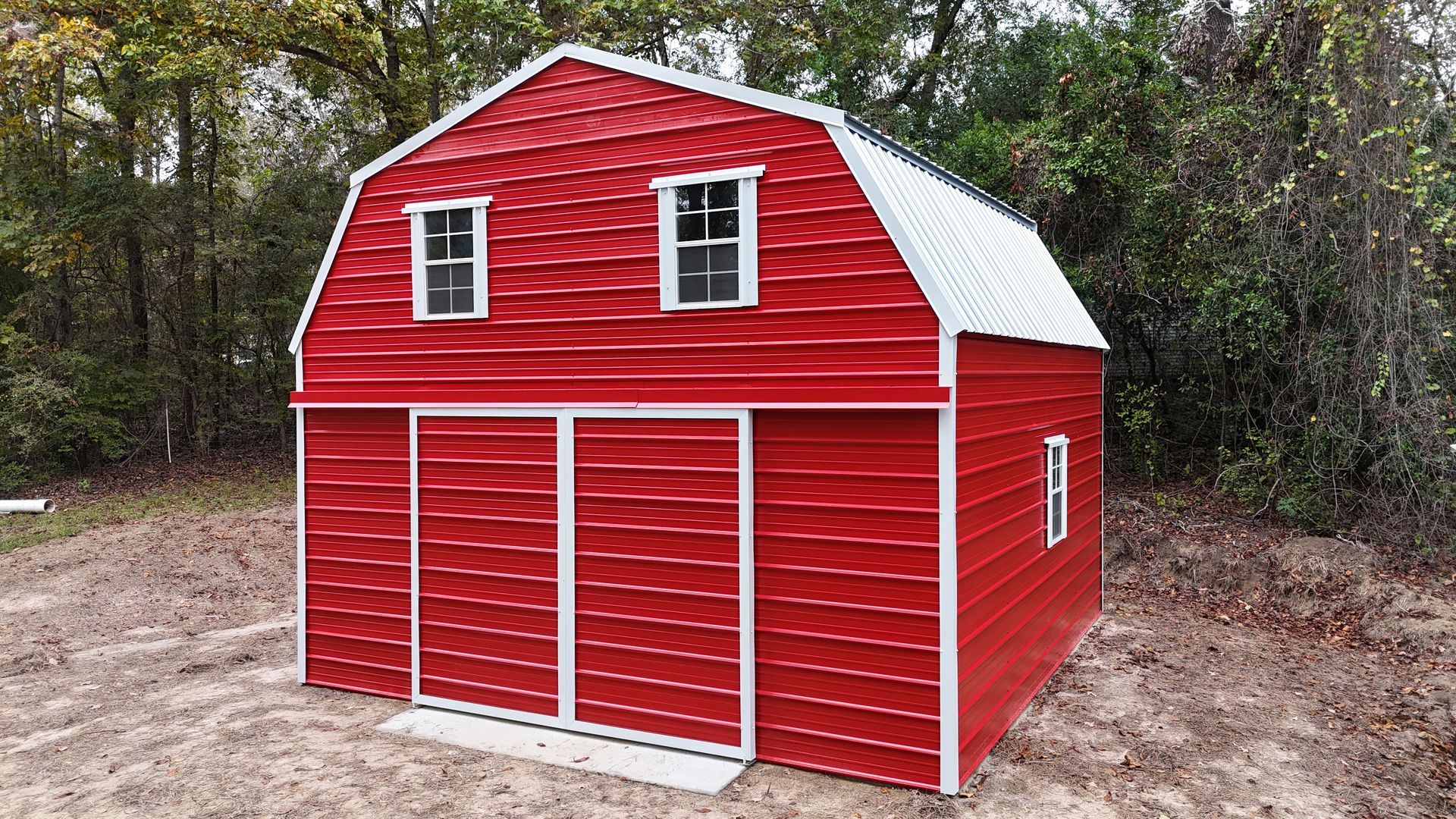 Red barn-style shed with white trim and a metal roof; two small windows on the upper level, two large doors on the lower level.