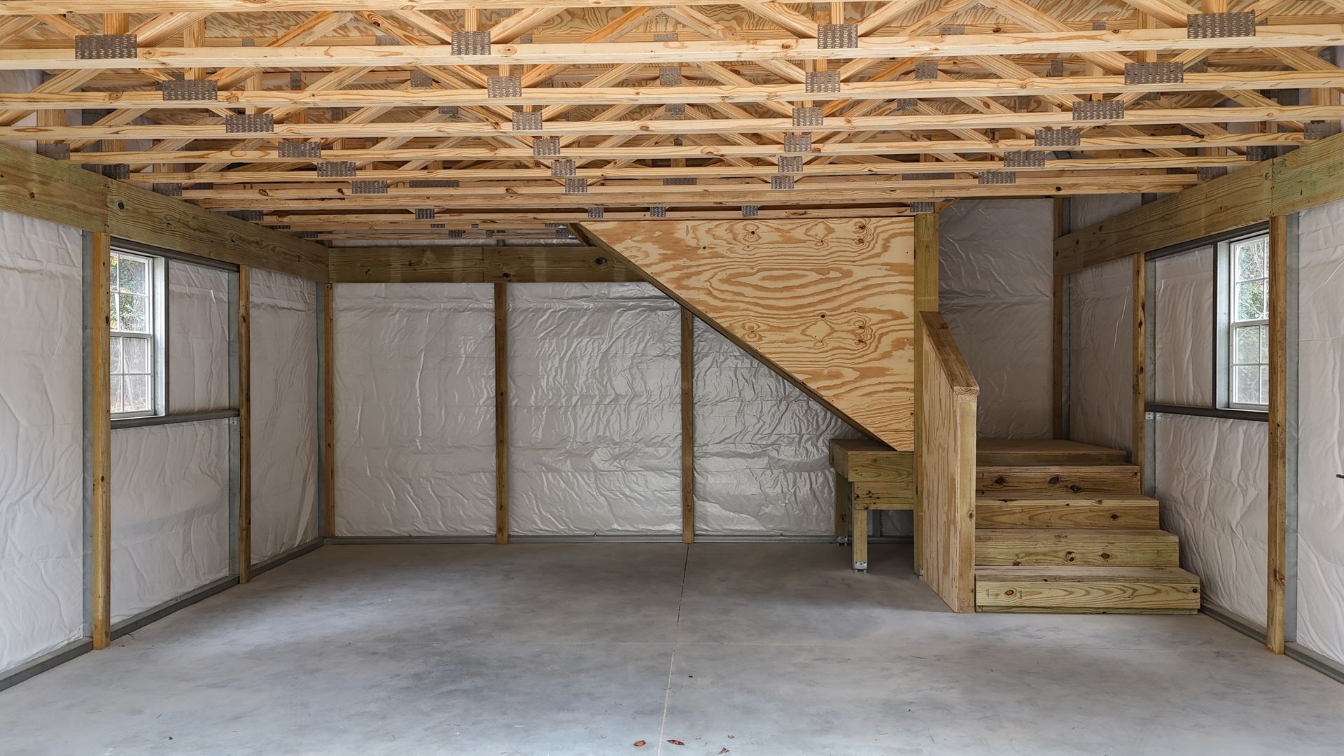 Interior of a building under construction, featuring a concrete floor, stairs, insulation, and wooden framework.