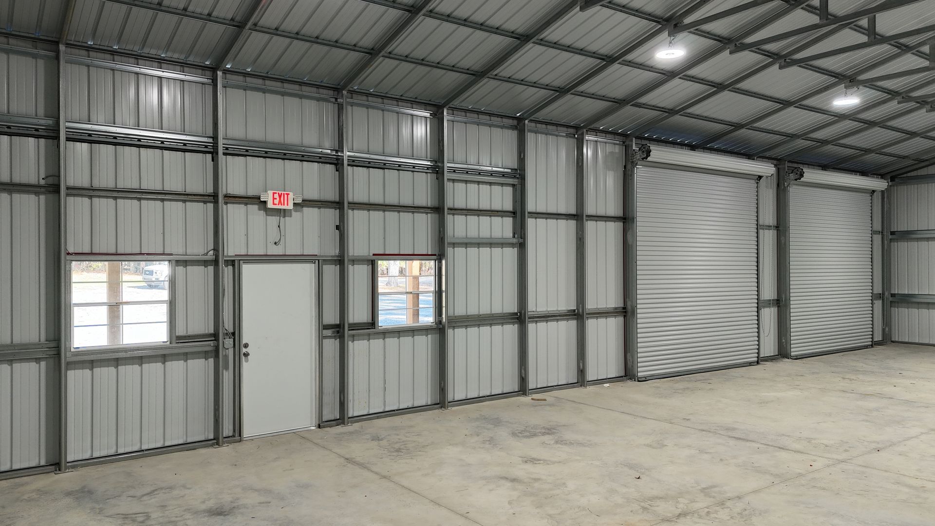 Interior of a metal industrial building with a door, window, and closed roll-up door.