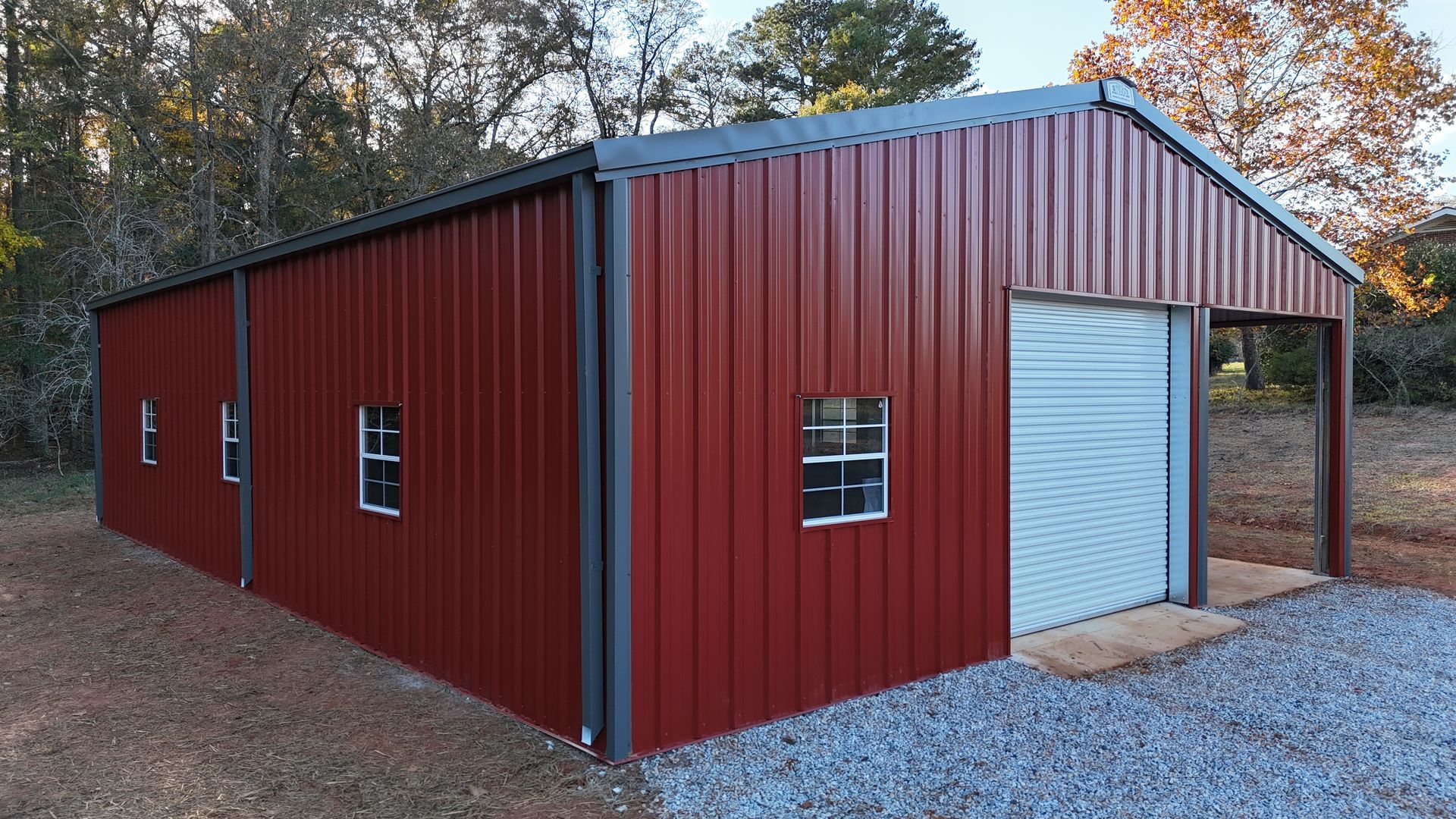 Red metal building with garage door and windows on a gravel lot.