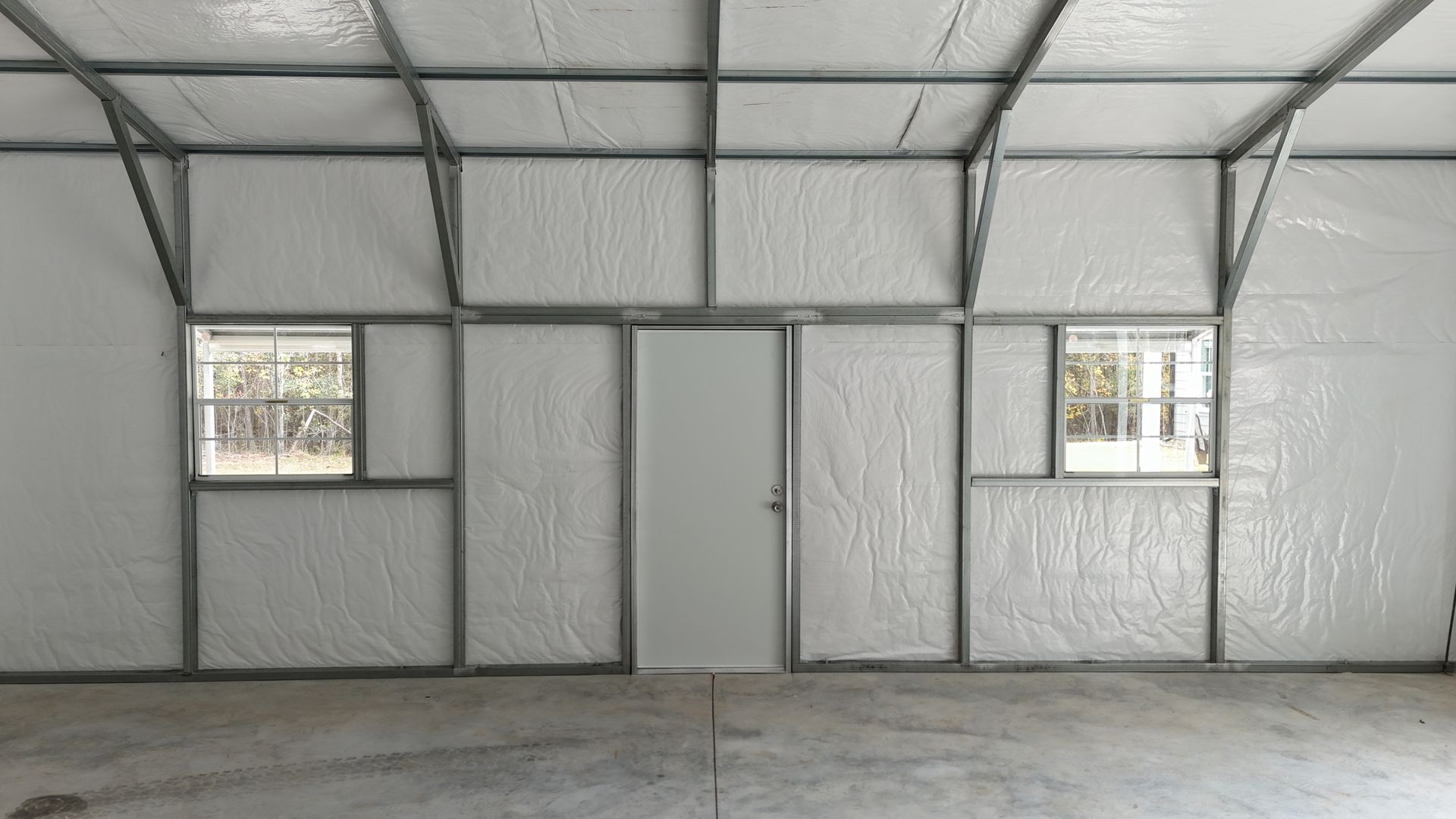 Interior of a metal framed building with windows and a door. Walls are covered in white insulation.