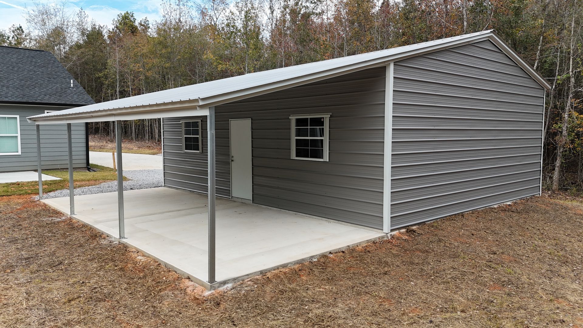 Gray metal building with attached porch; concrete patio, white door, windows.