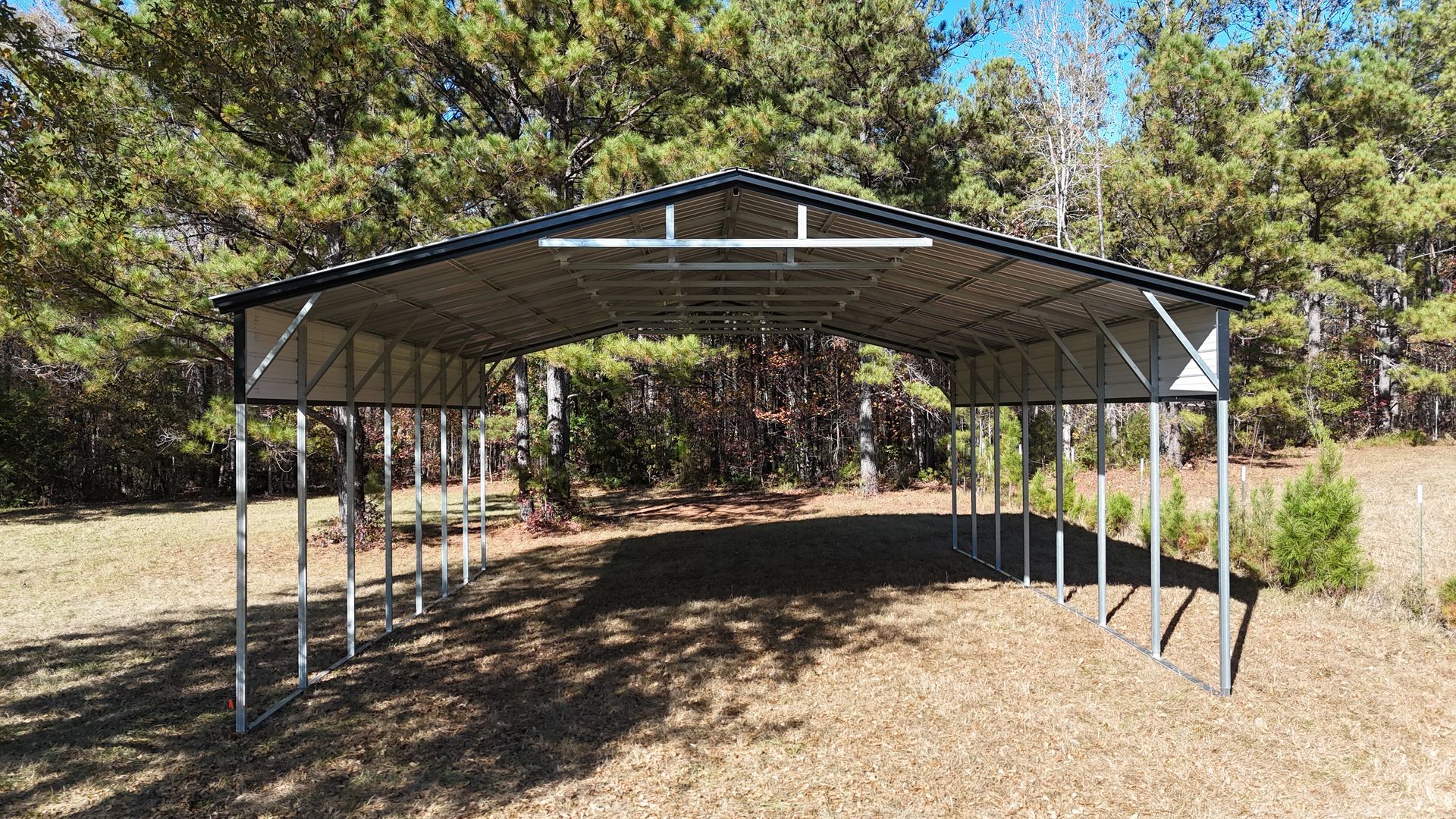 Metal carport in a wooded area, with a black roof and silver frame.