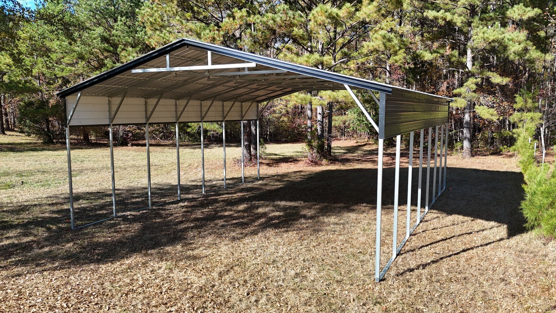 Metal carport structure in a grassy area, with a wooded background.