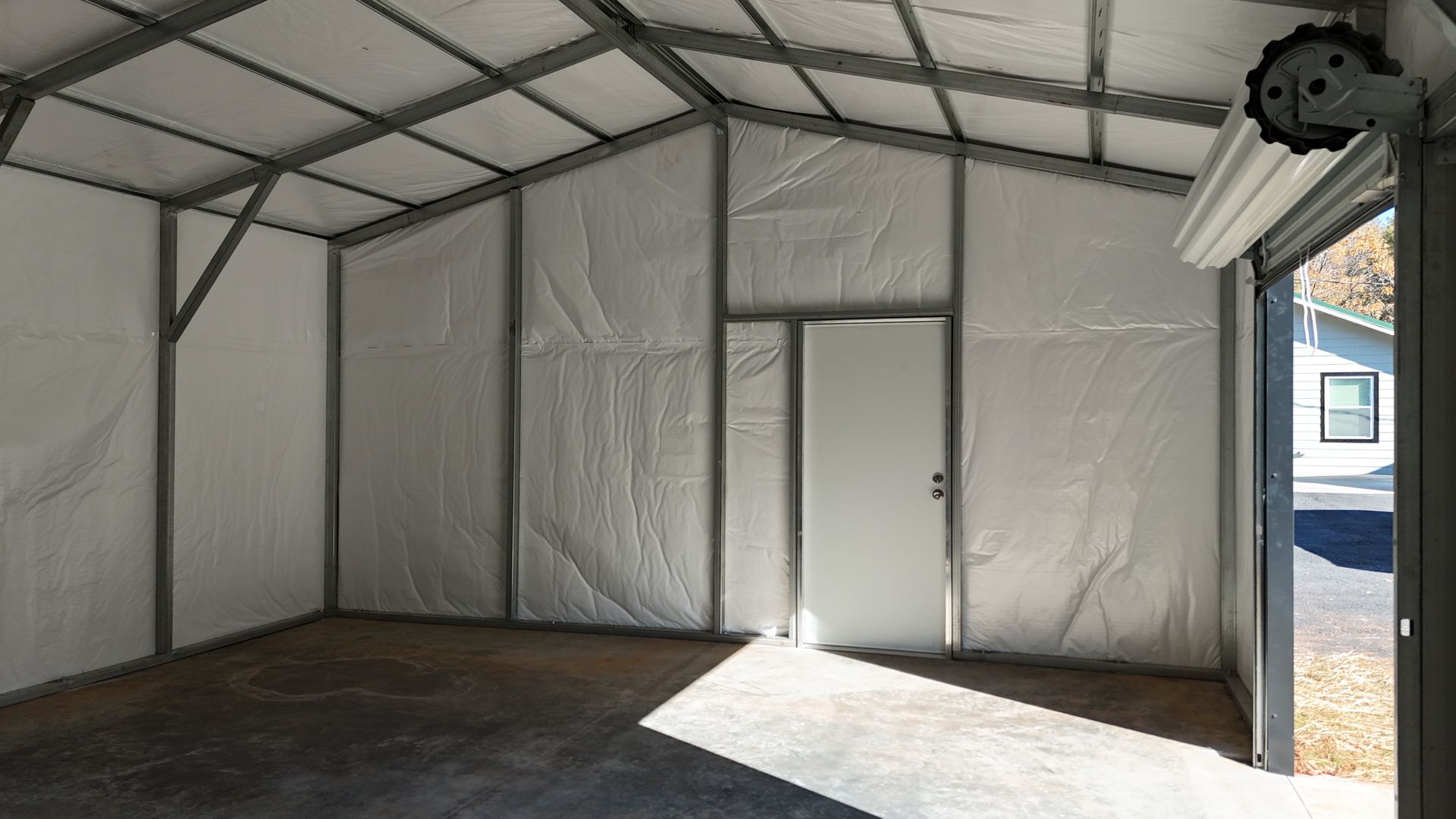 Interior of a metal framed building with white walls, a concrete floor, and an open garage door.