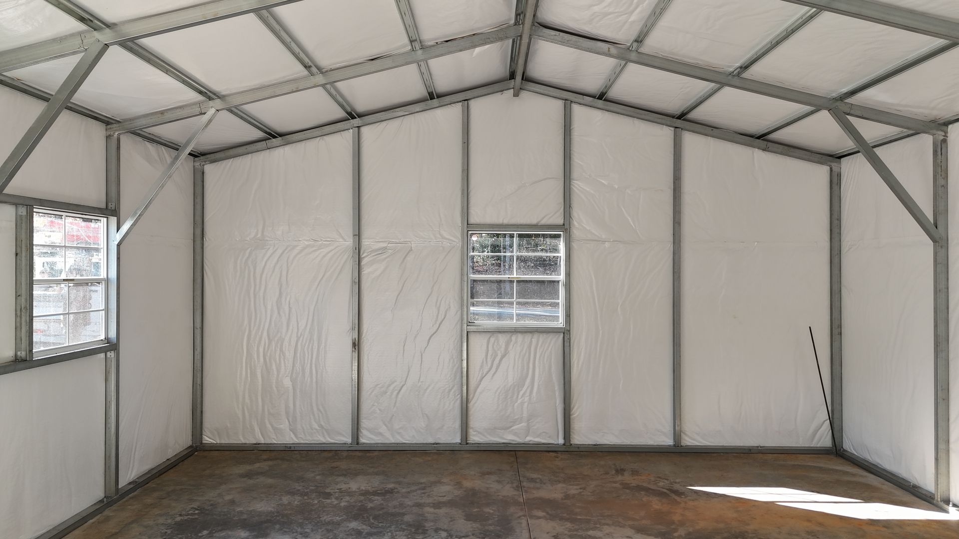 Interior of a metal framed structure with white panel walls and windows; concrete floor.