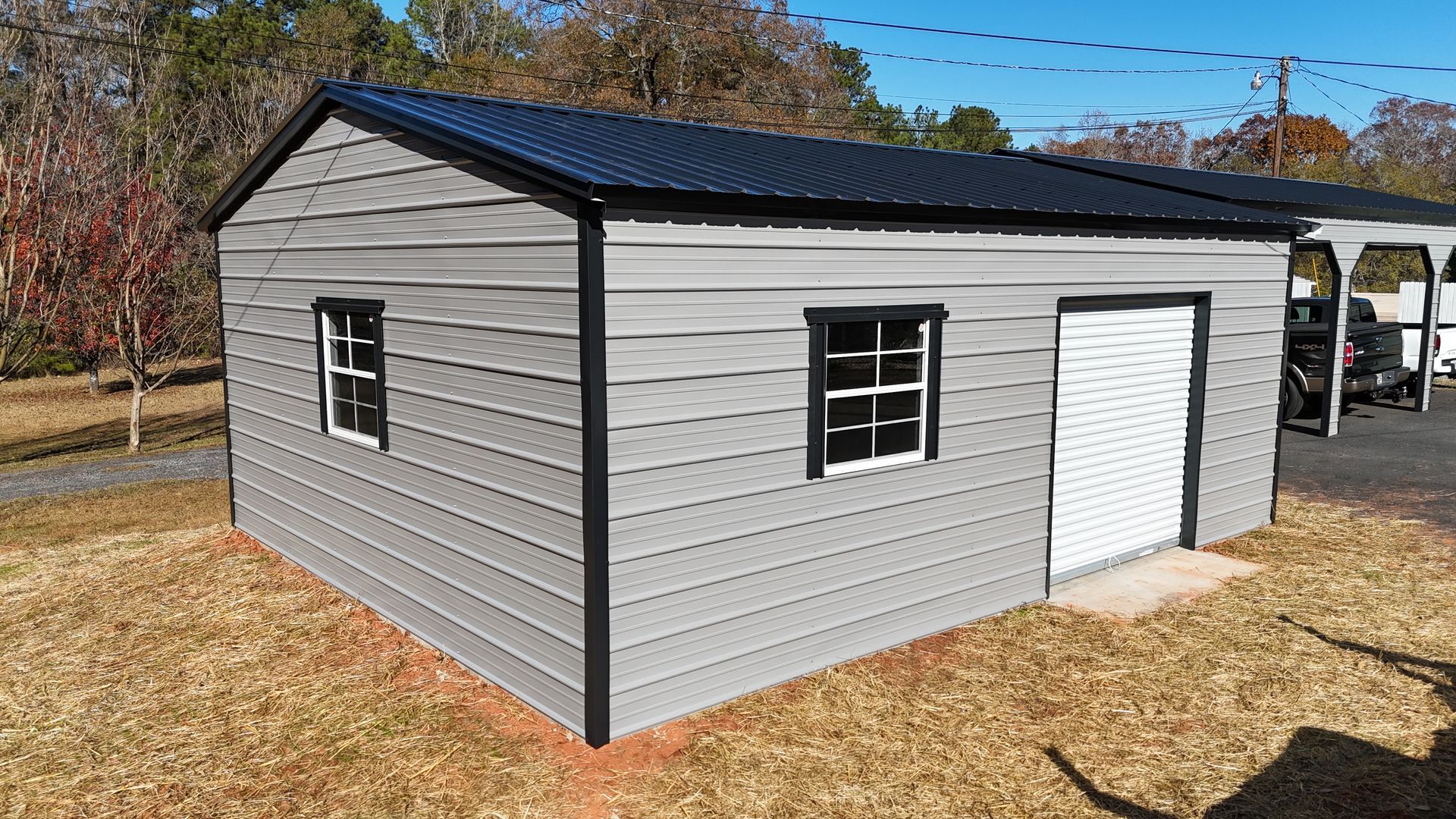 Gray metal shed with black trim and roof, two windows, and a door, set on brown grass.