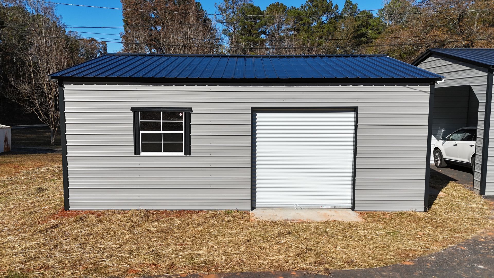 Gray metal building with blue roof, white garage door, and small window.