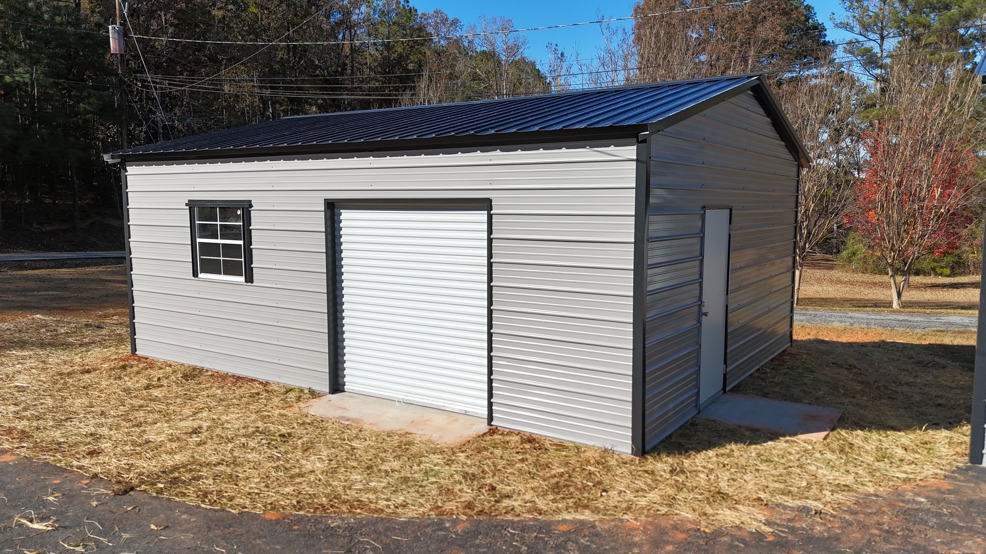 Gray metal shed with black roof, white door, and small window on a grassy area.