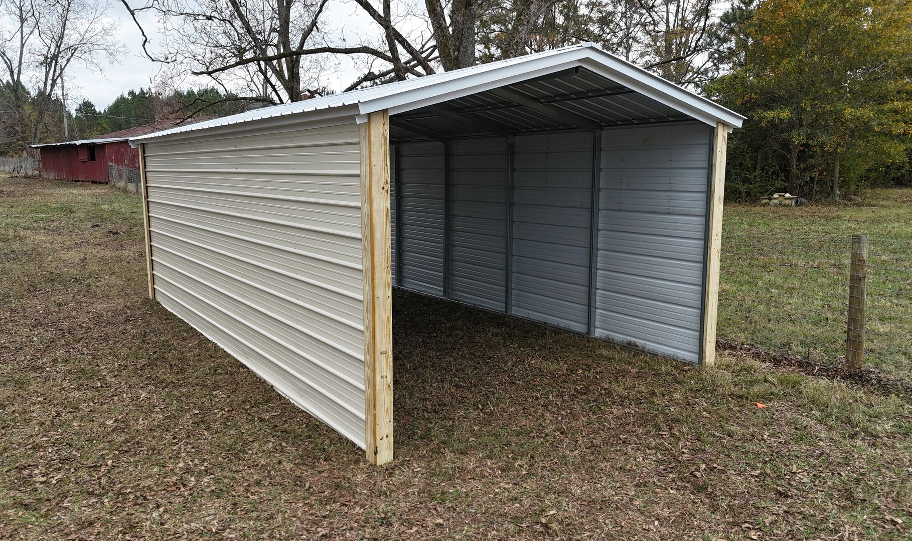 Tan metal carport on a grassy lot, with wooden posts and a white roof.