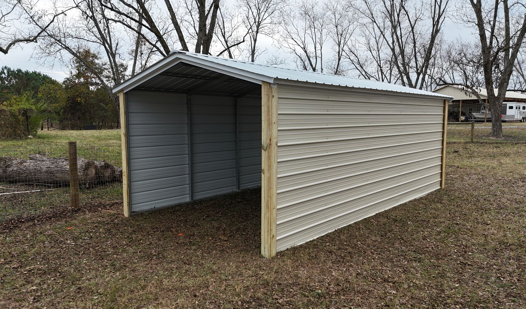 Metal carport with light-colored siding, open on one side, sitting on a grassy yard.
