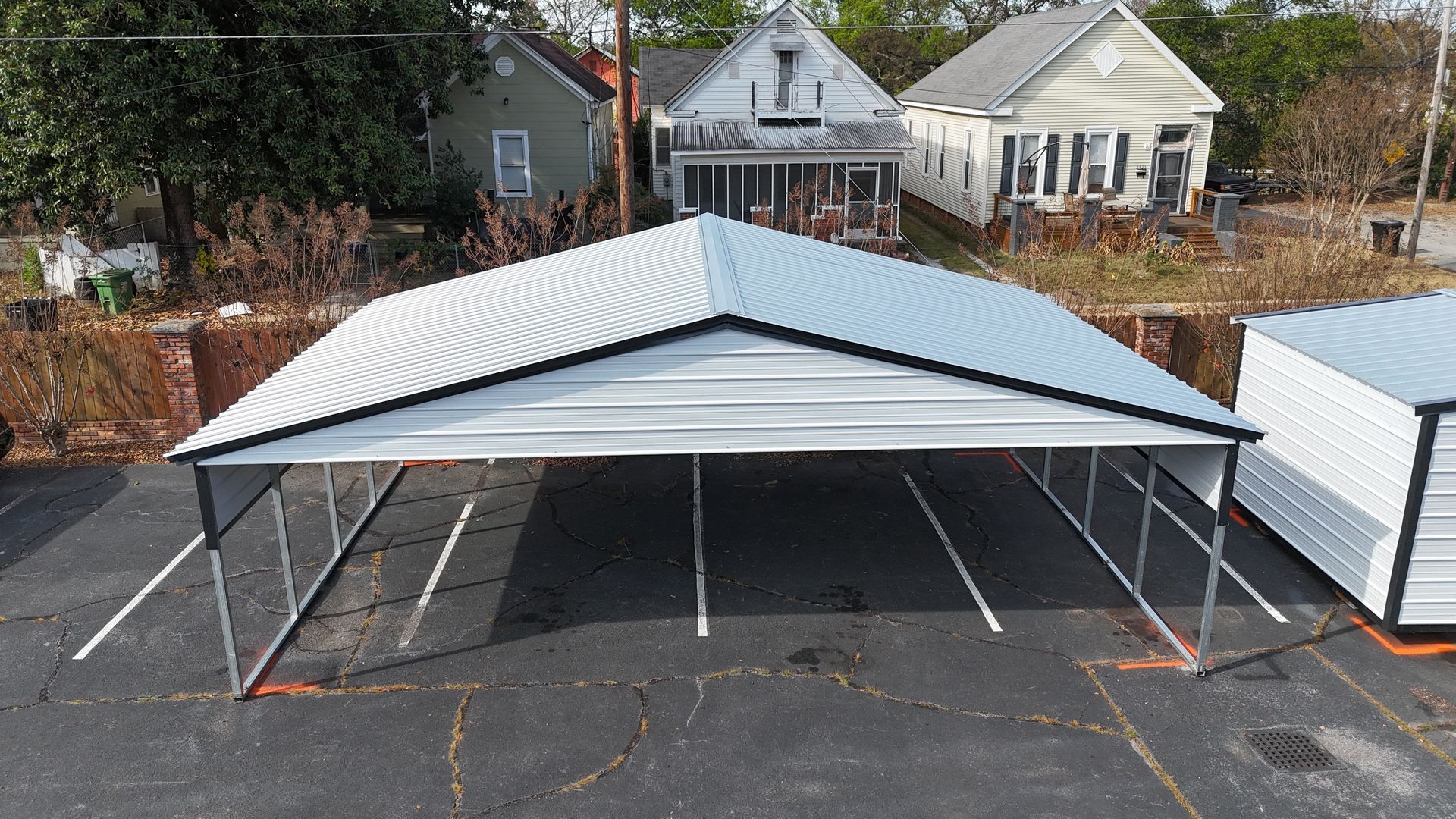 A white carport with a corrugated roof over parking spaces. Buildings are in the background.