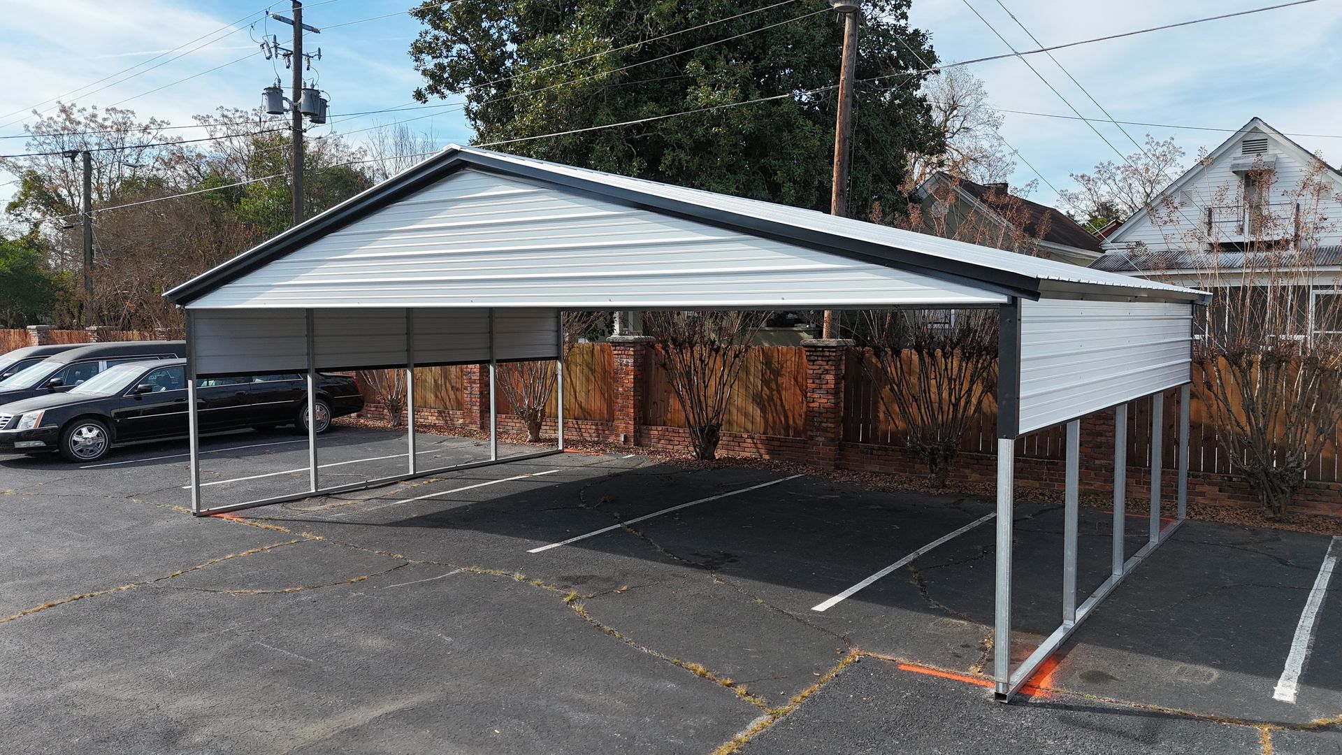 Metal carport in parking lot, covering several parking spaces. Gray and white colors.