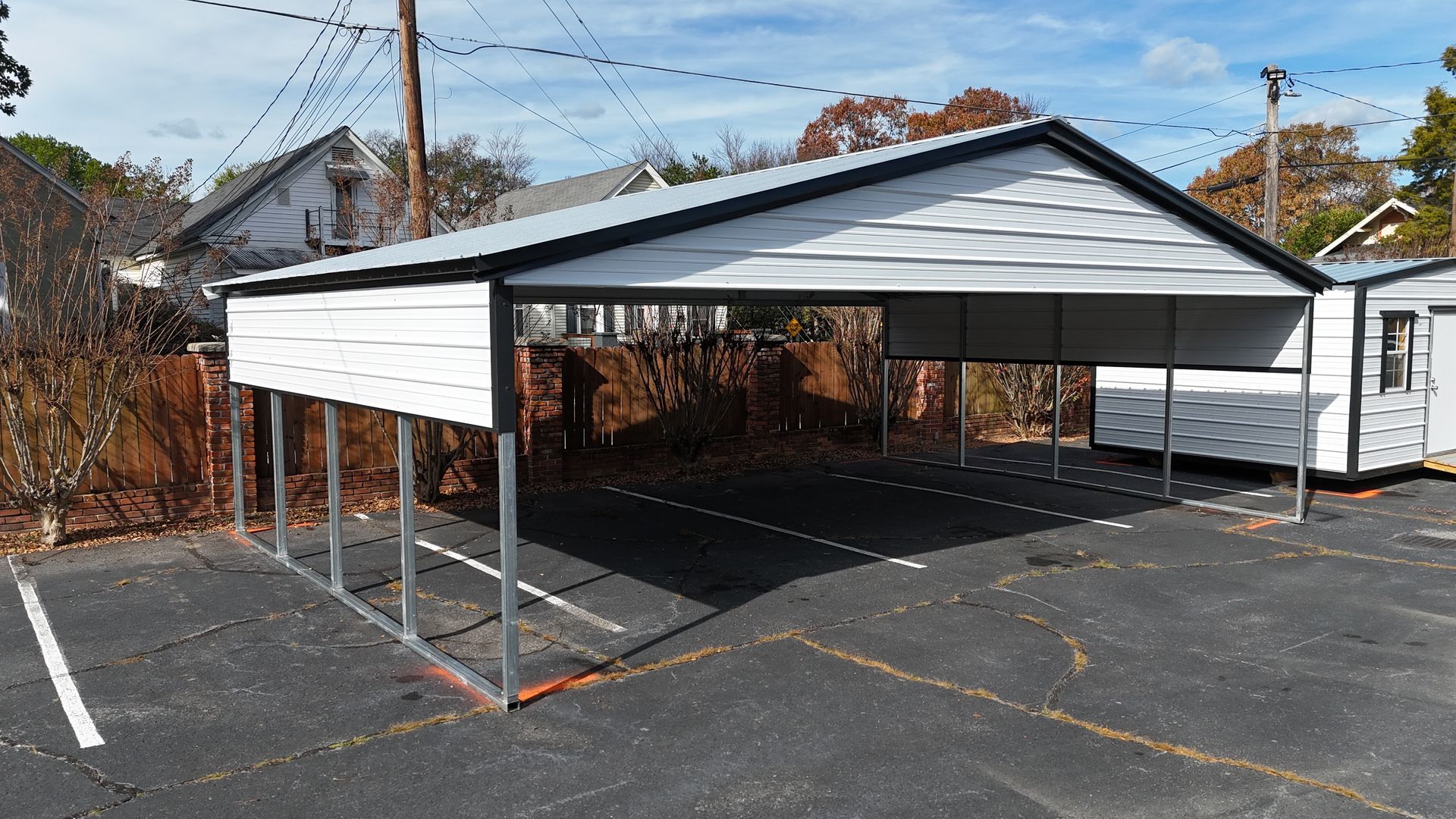 White and gray carport with metal roof, erected on asphalt parking area.