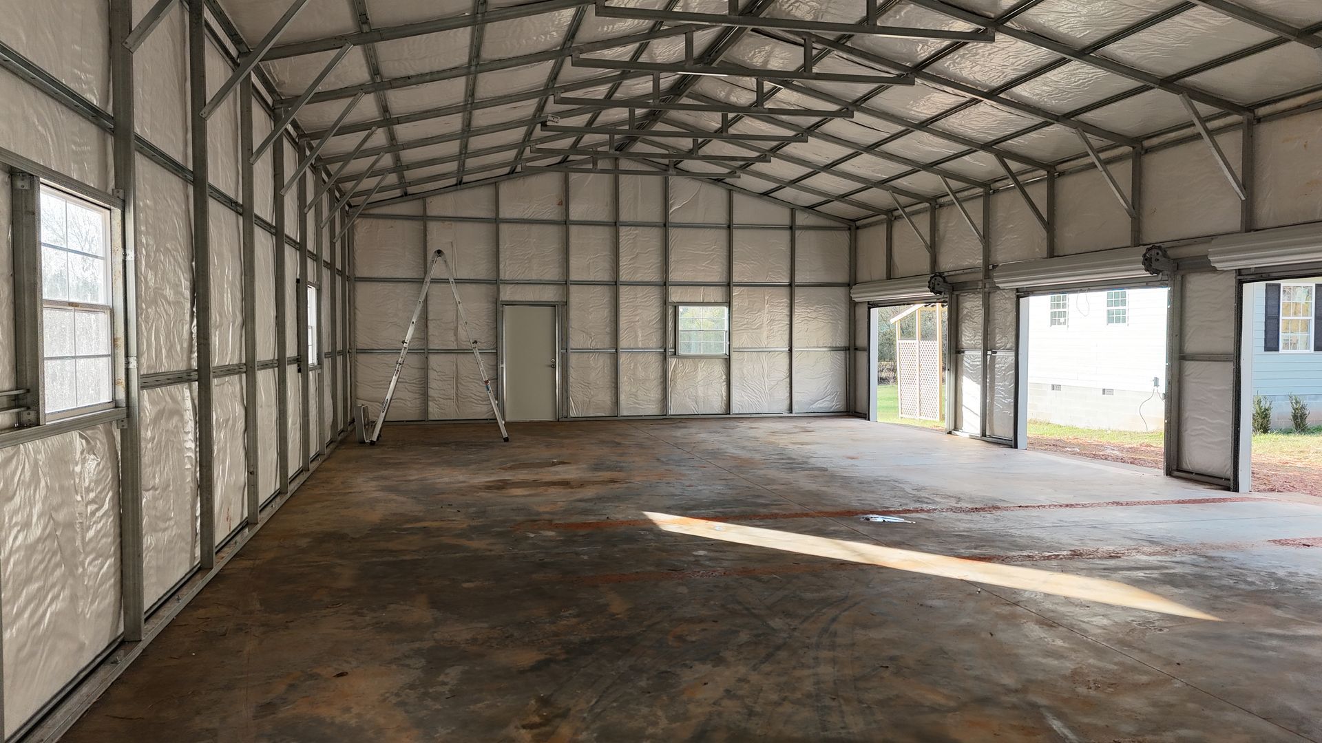 Interior of a metal framed building with concrete floor, windows, door, and garage doors.