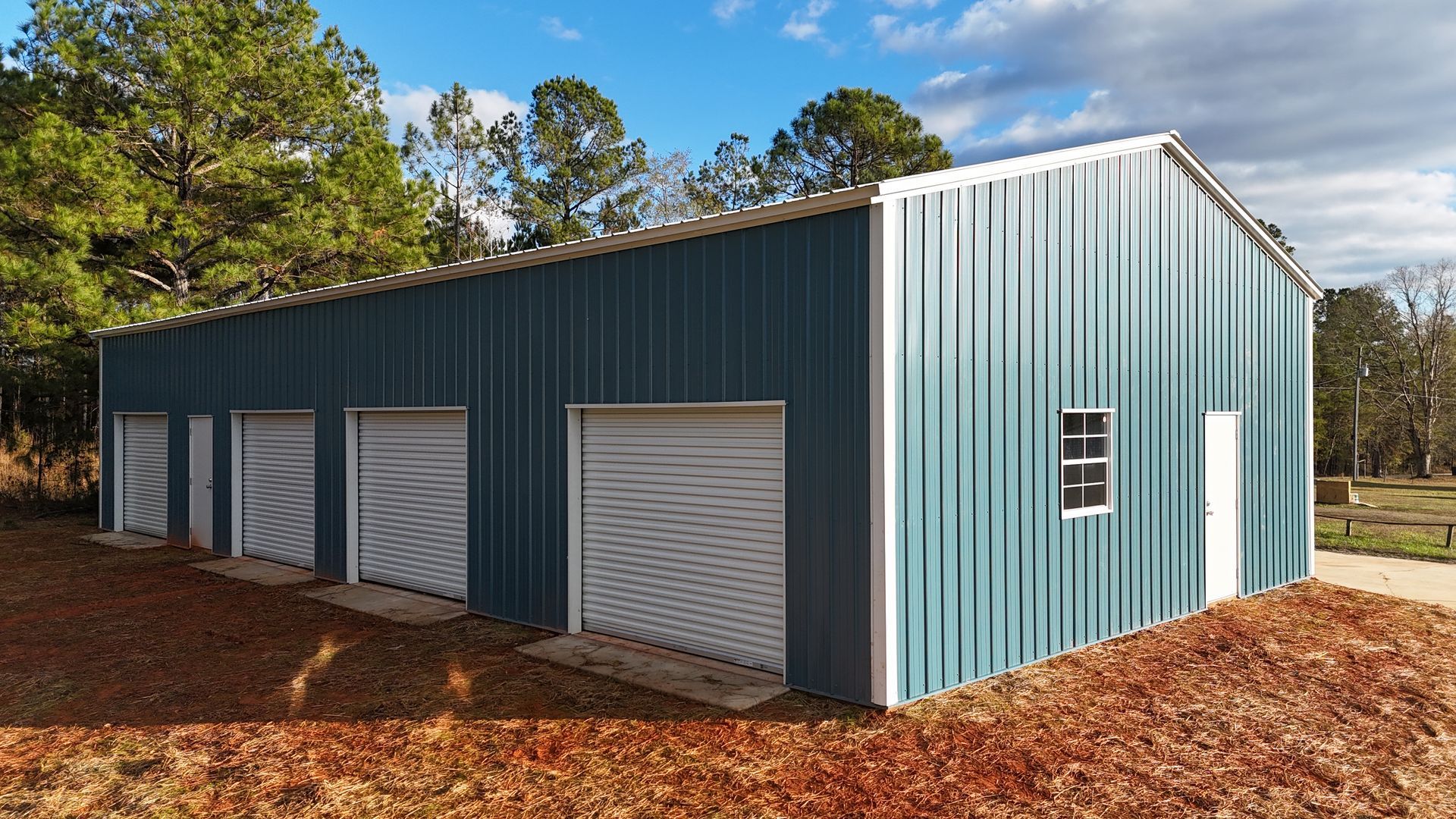 Blue metal building with several garage doors and a small window in a rural setting.