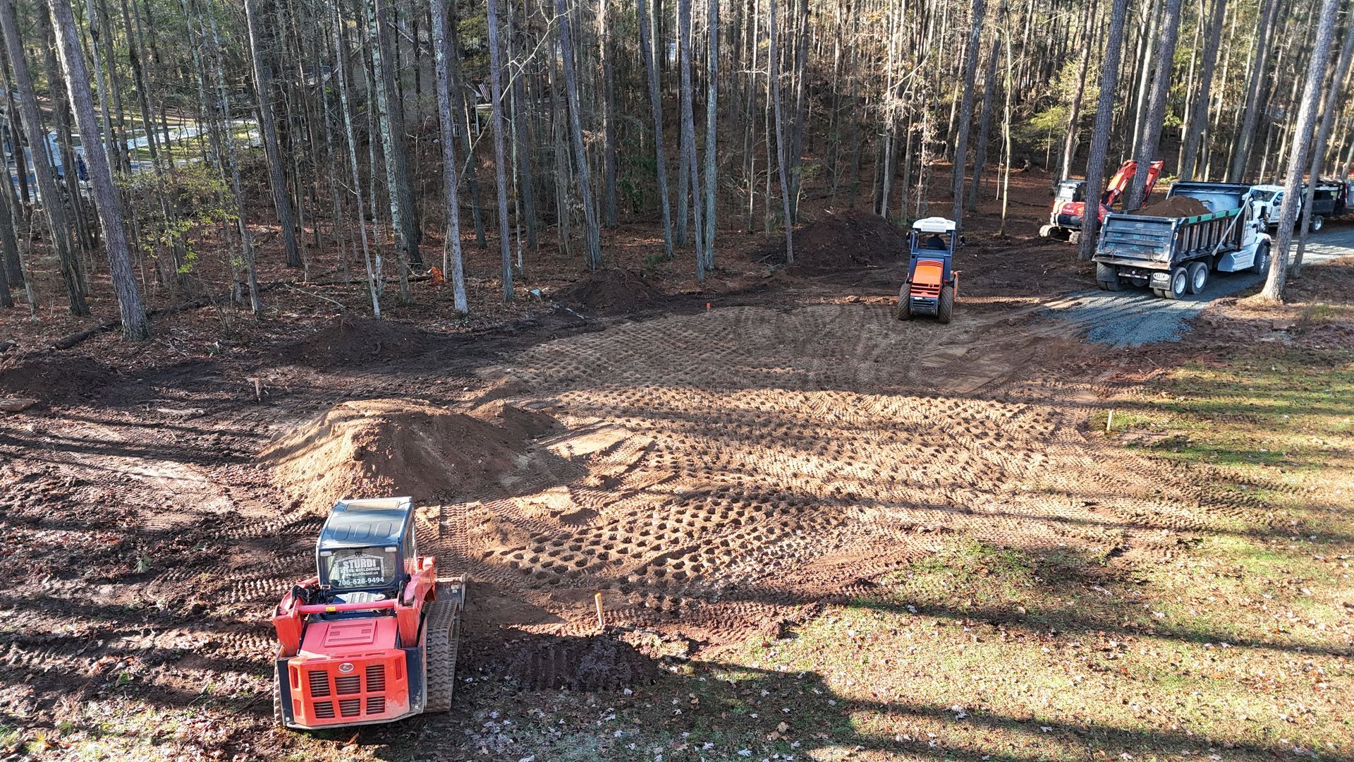 Construction site with orange skid steers clearing land near a forest.