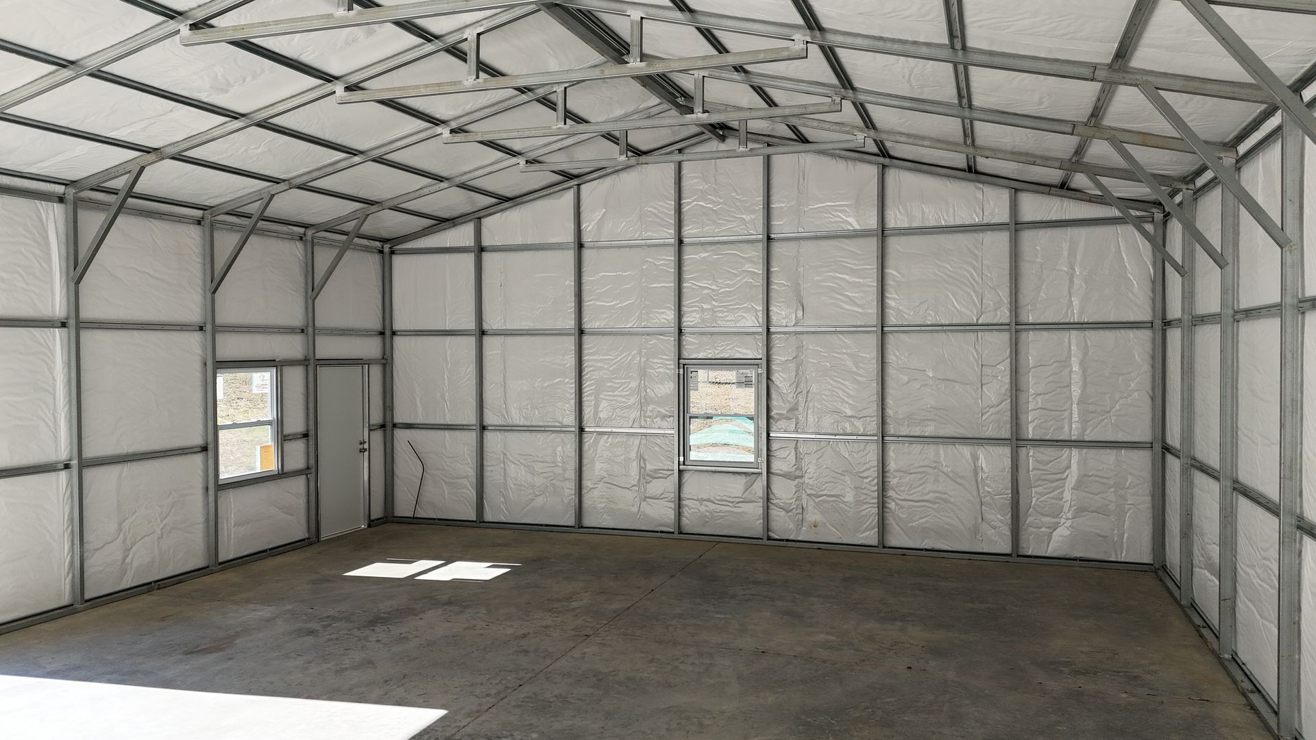 Interior of a metal framed building with insulation on walls and roof, concrete floor, door and windows.