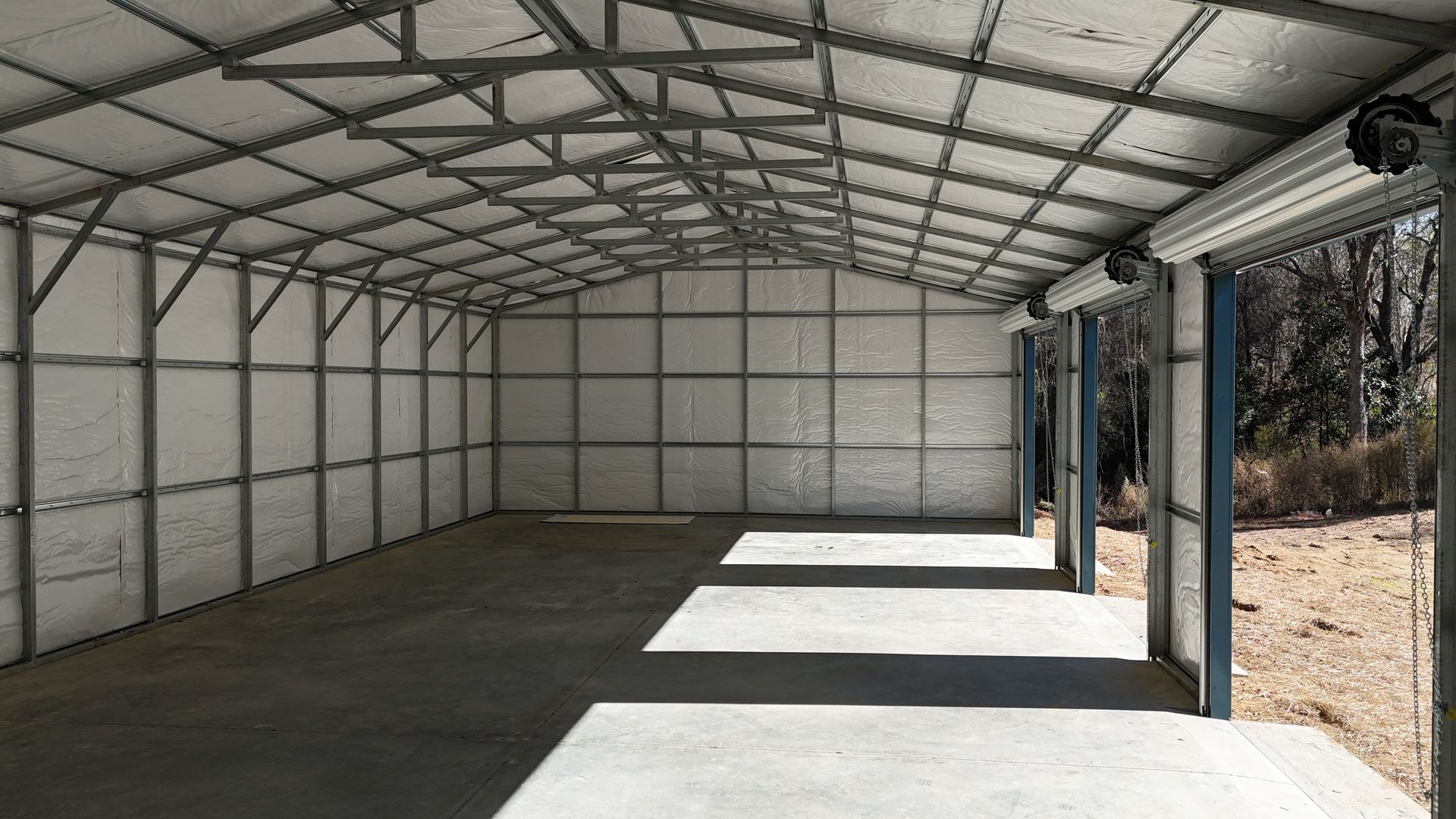 Interior view of a metal-framed garage with a concrete floor, open door, and white walls.