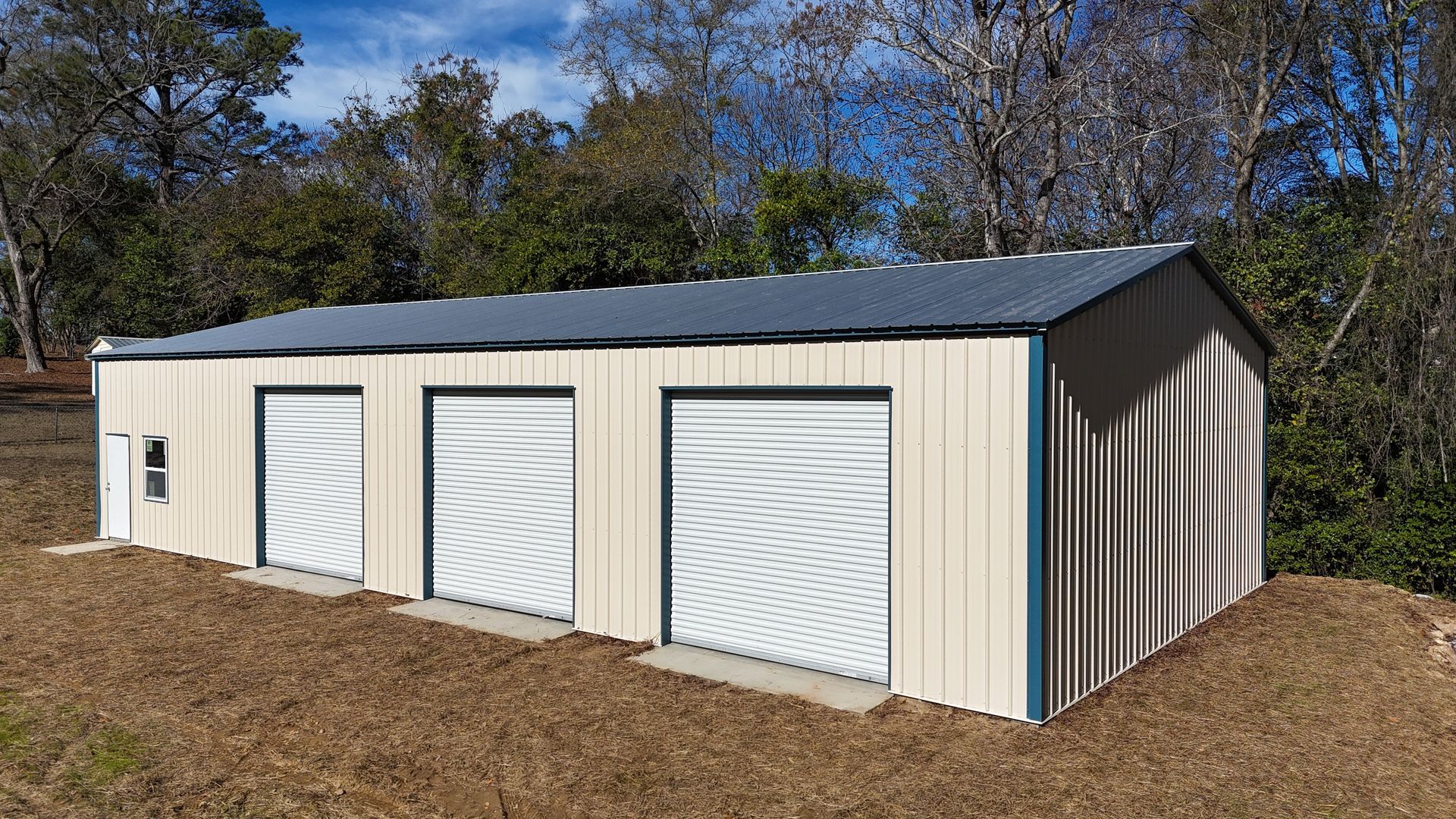 Three-bay metal storage building with roll-up doors, beige siding, and a blue roof, situated outdoors with trees.