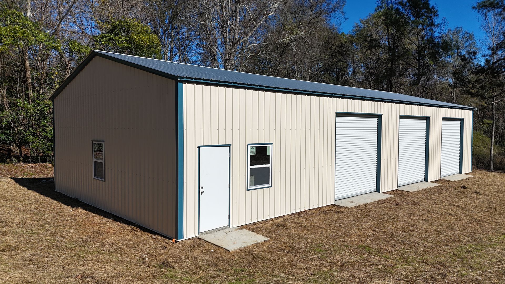 Tan metal building with blue trim, three garage doors, a door, and a window.
