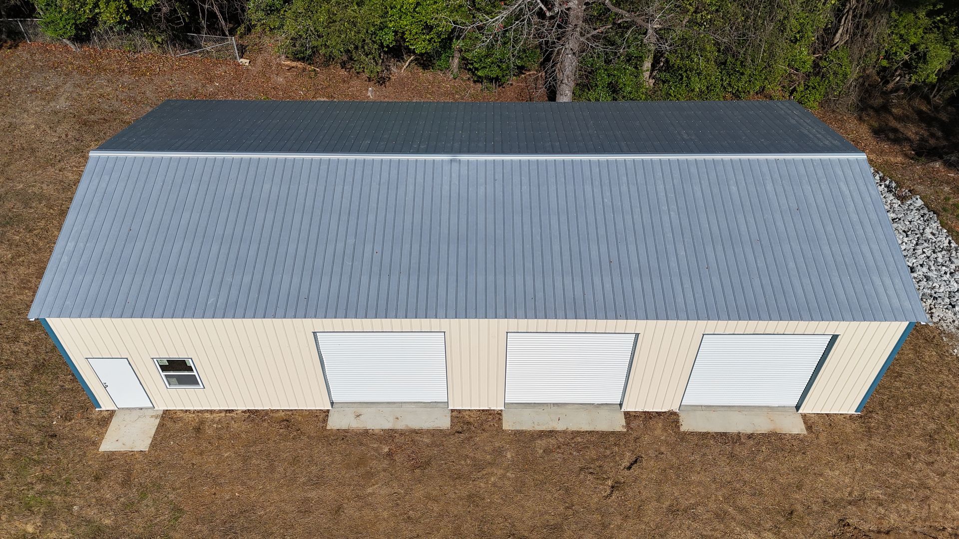 Beige three-bay garage with gray roof and white garage doors, set in a grassy outdoor area.