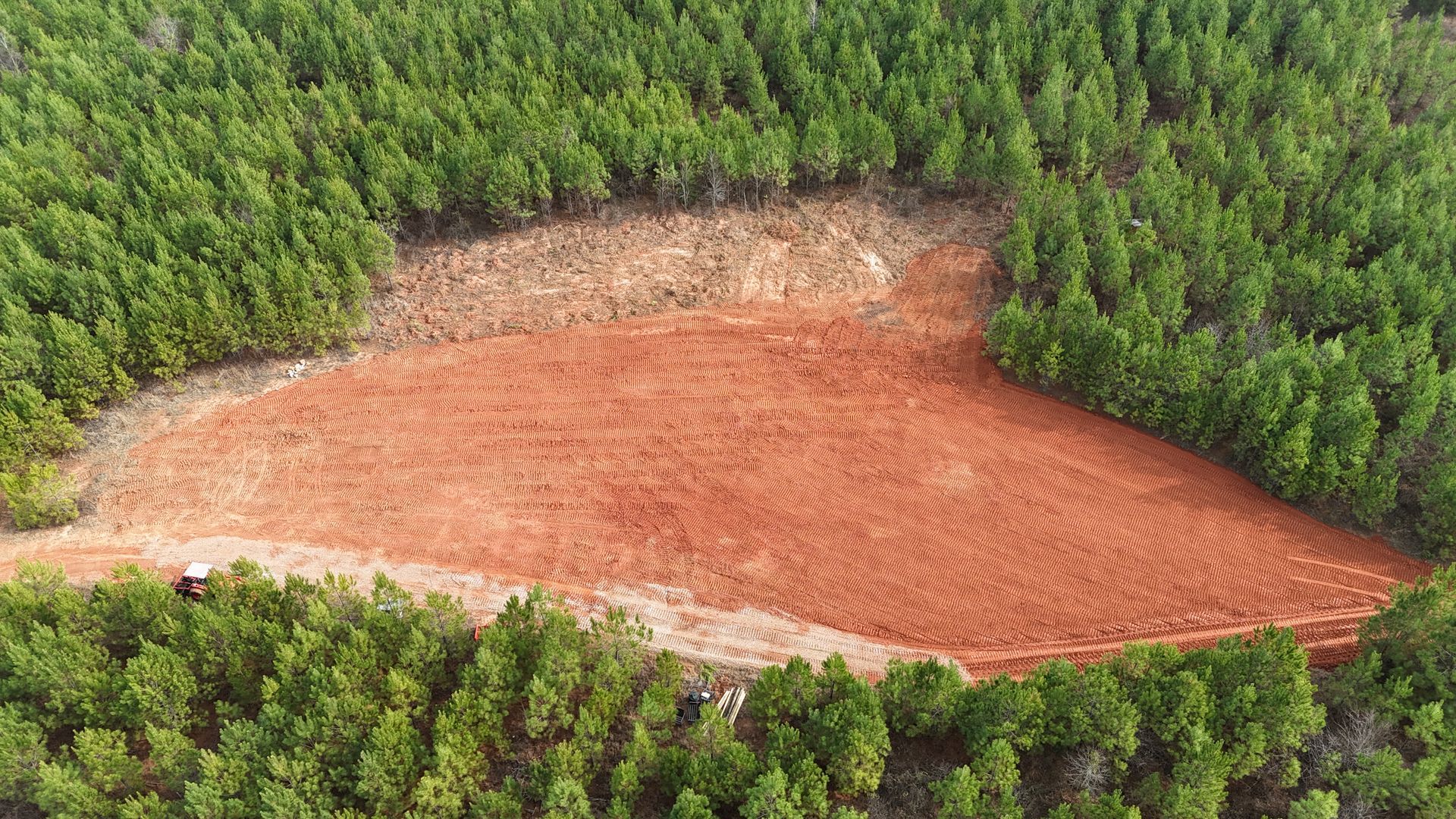 Aerial view of deforestation. Red soil clearing surrounded by green forest.
