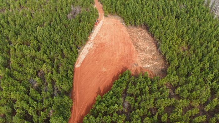 Aerial view of a deforested area with a wide, red-brown path cleared through a green forest.