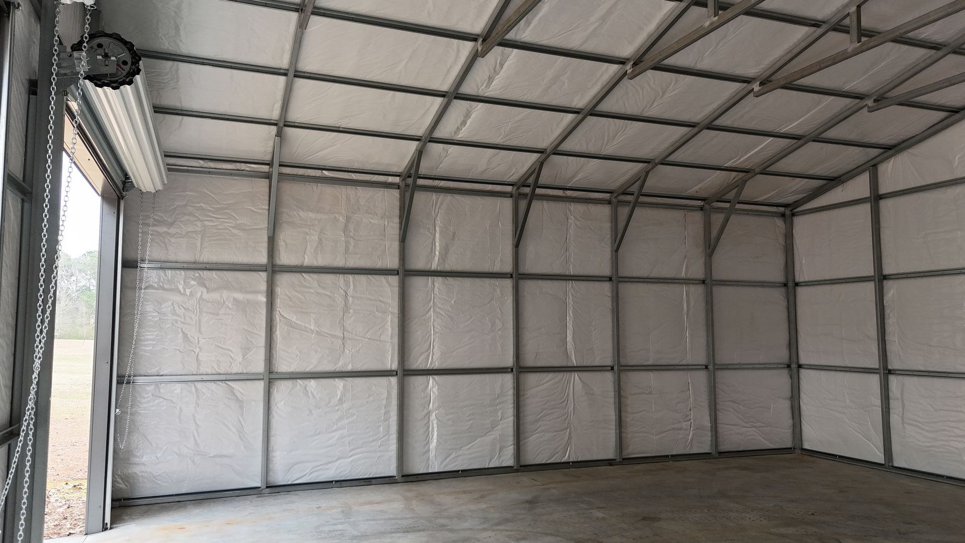 Interior of a metal building with a roll-up door, metal frame walls, and a curved ceiling.