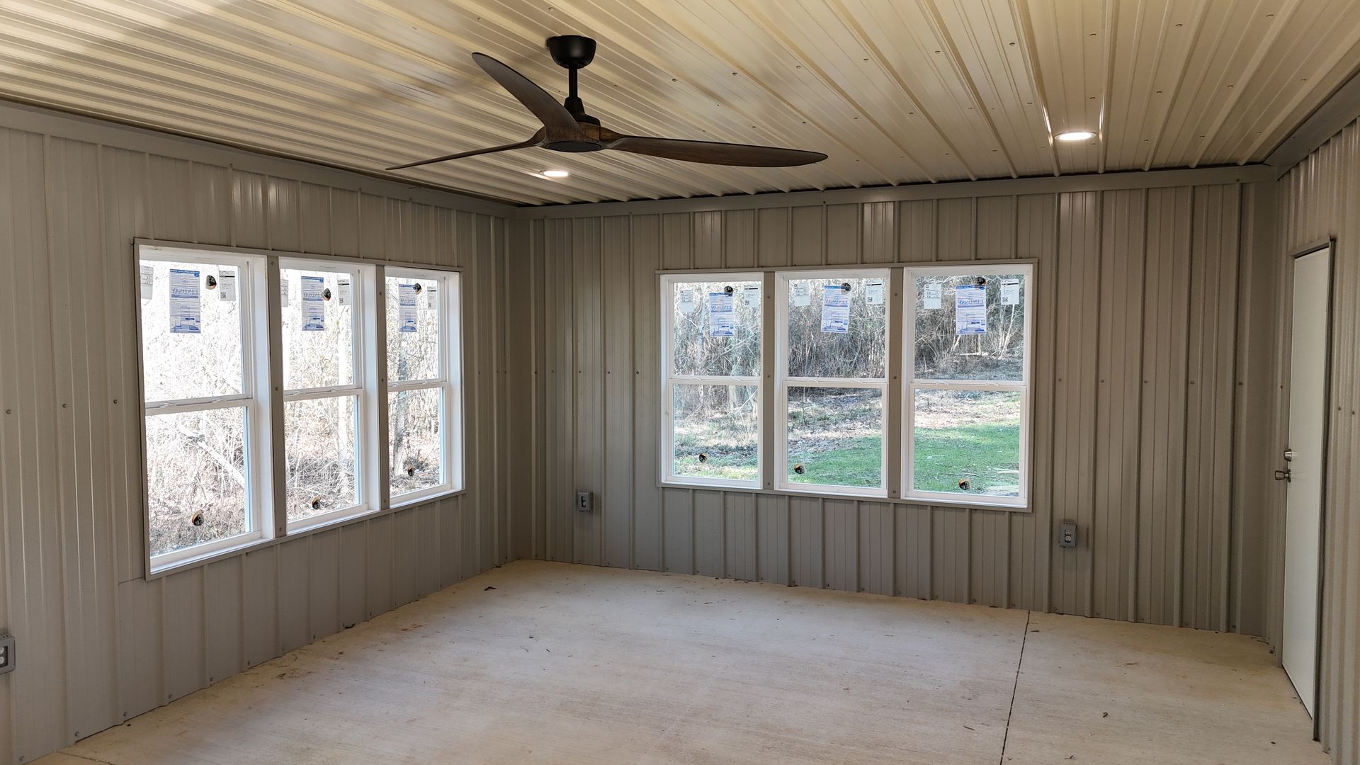 Interior of a room with metal walls, windows, and ceiling. A ceiling fan and lights are installed.